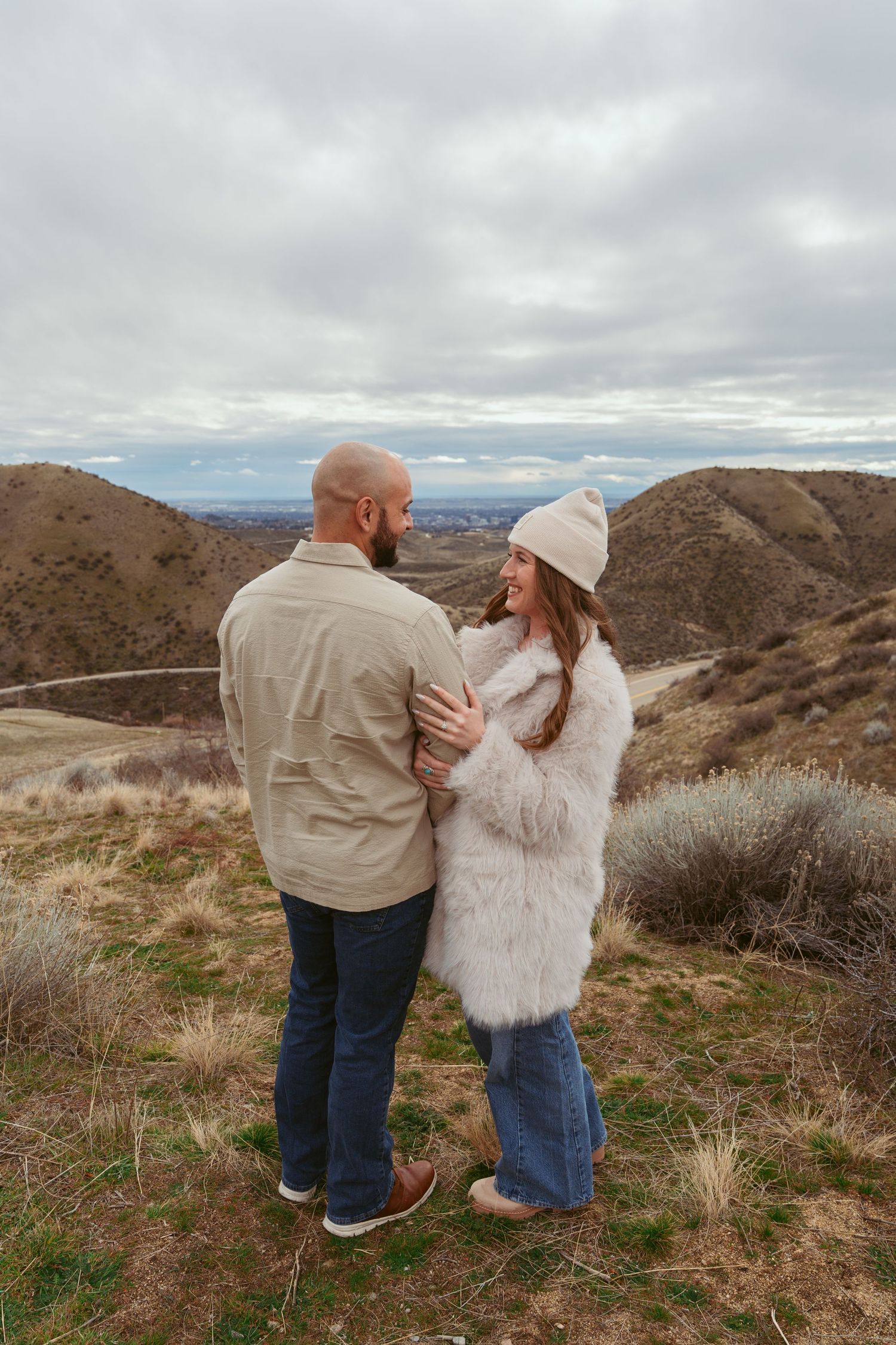 A couple shares an intimate moment while standing on a hilltop overlooking a mountain landscape.