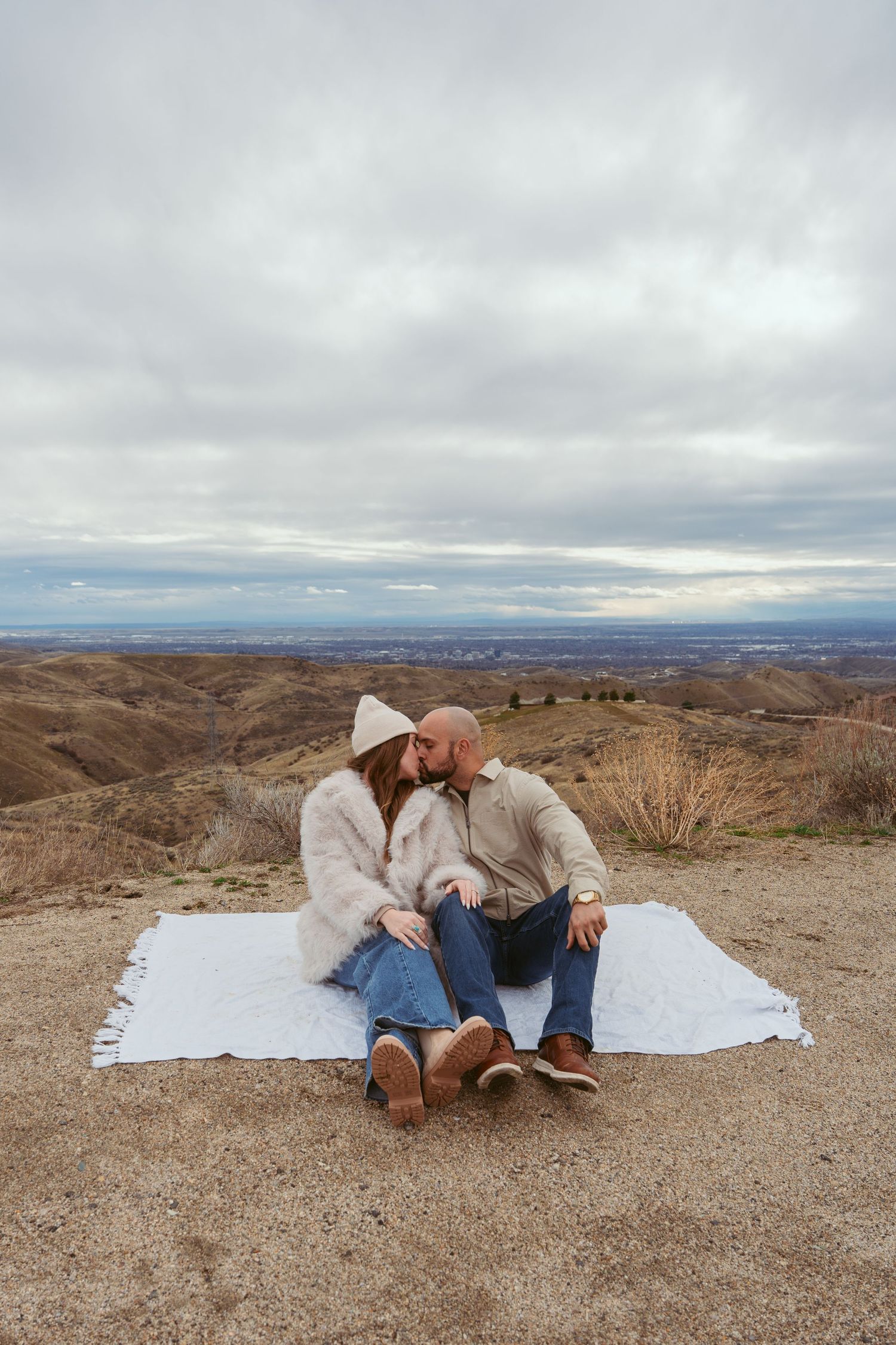 Couple lying on white blanket overlooking desert mountain landscape.