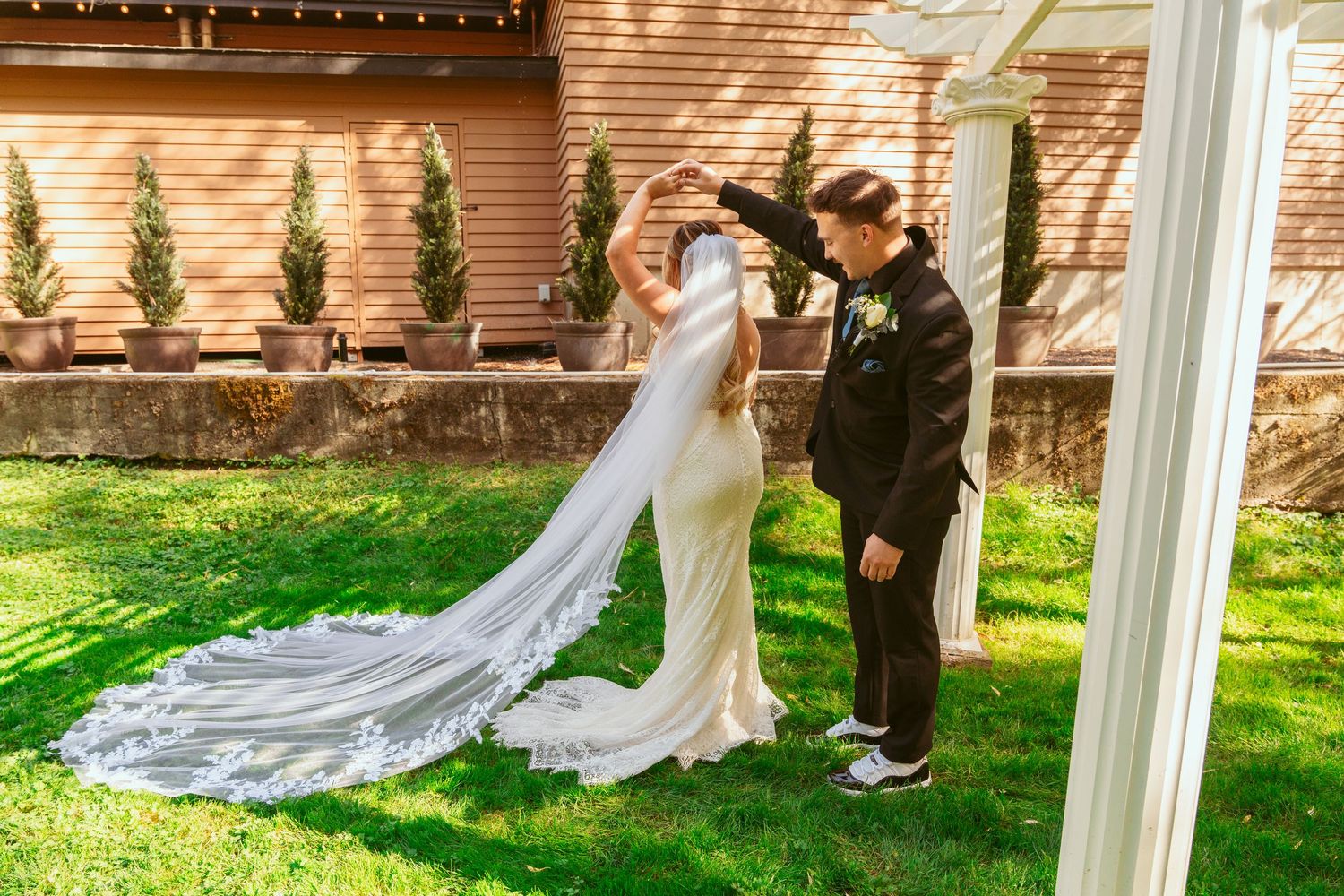 Wedding ceremony setup with white pillars and string lights in a sunlit garden setting.
