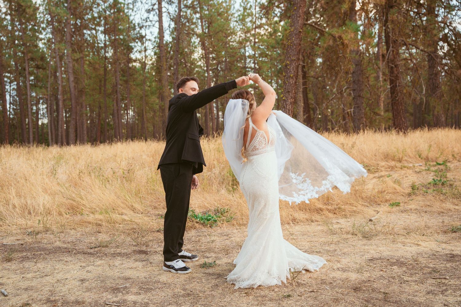 A wedding couple poses playfully in a rustic outdoor setting with tall pine trees.