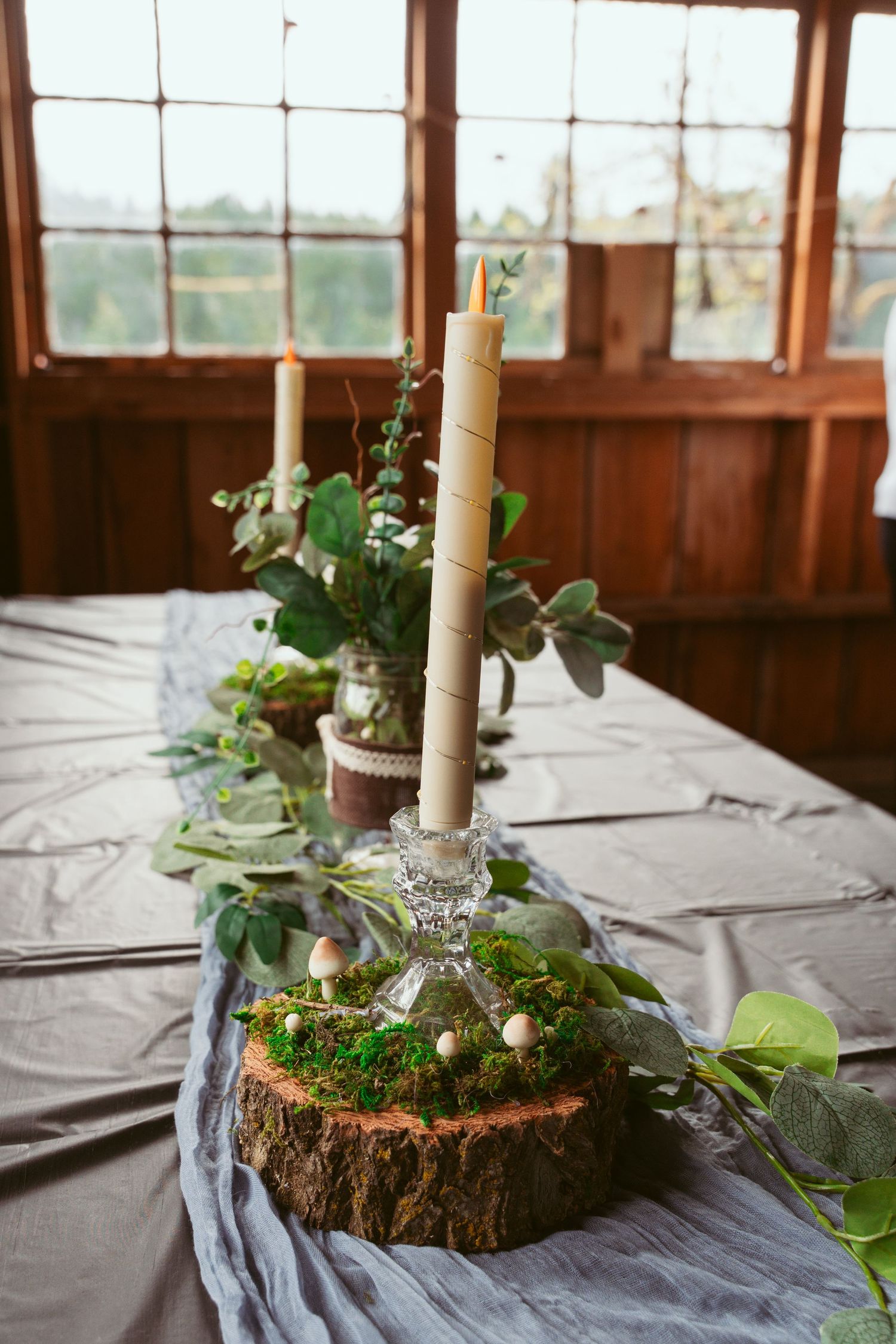 Rustic centerpiece featuring wood slices, white candles, and fresh greenery on reception tables.