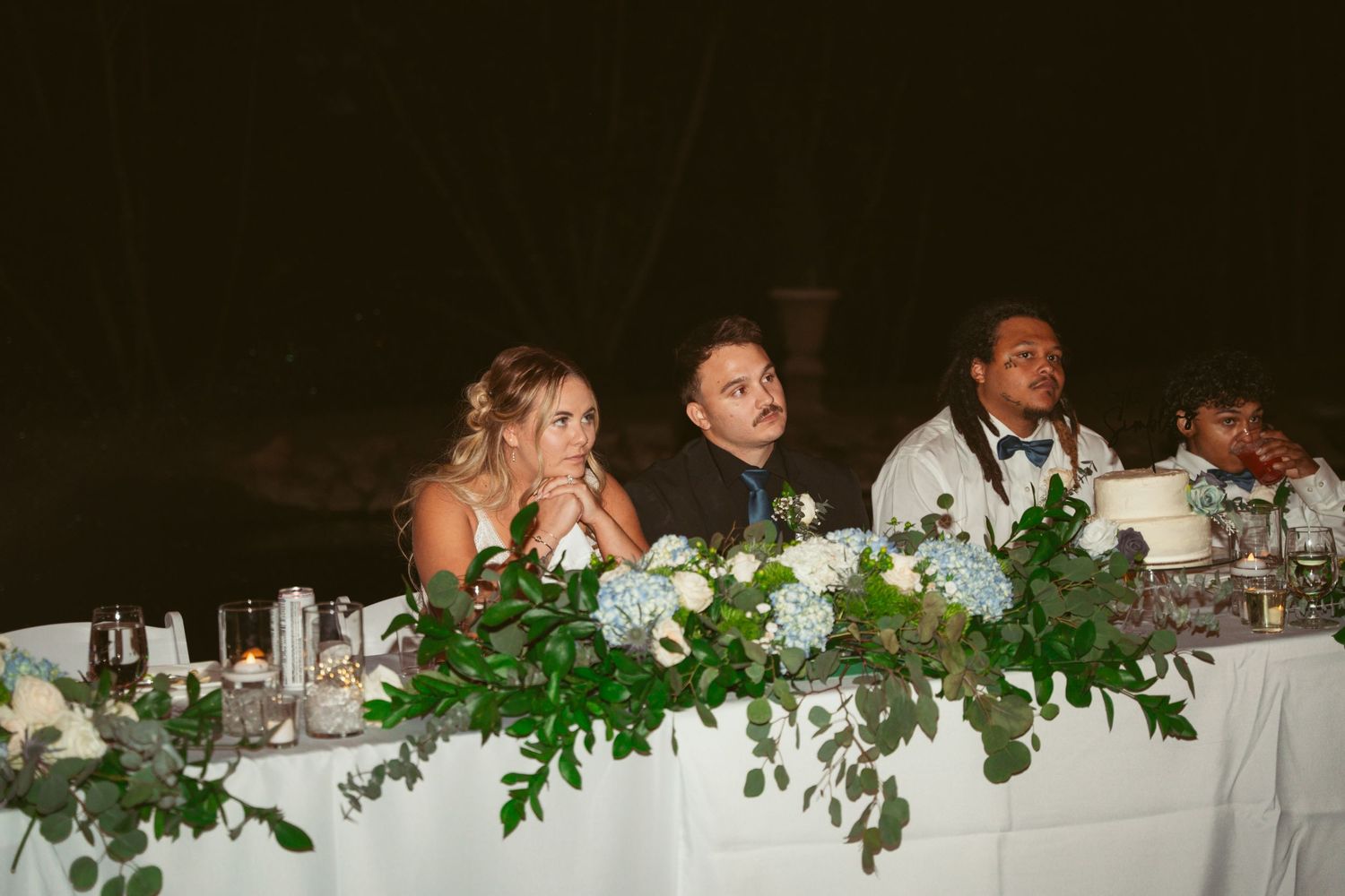 Head table decorated with elegant greenery garlands at an outdoor wedding reception.