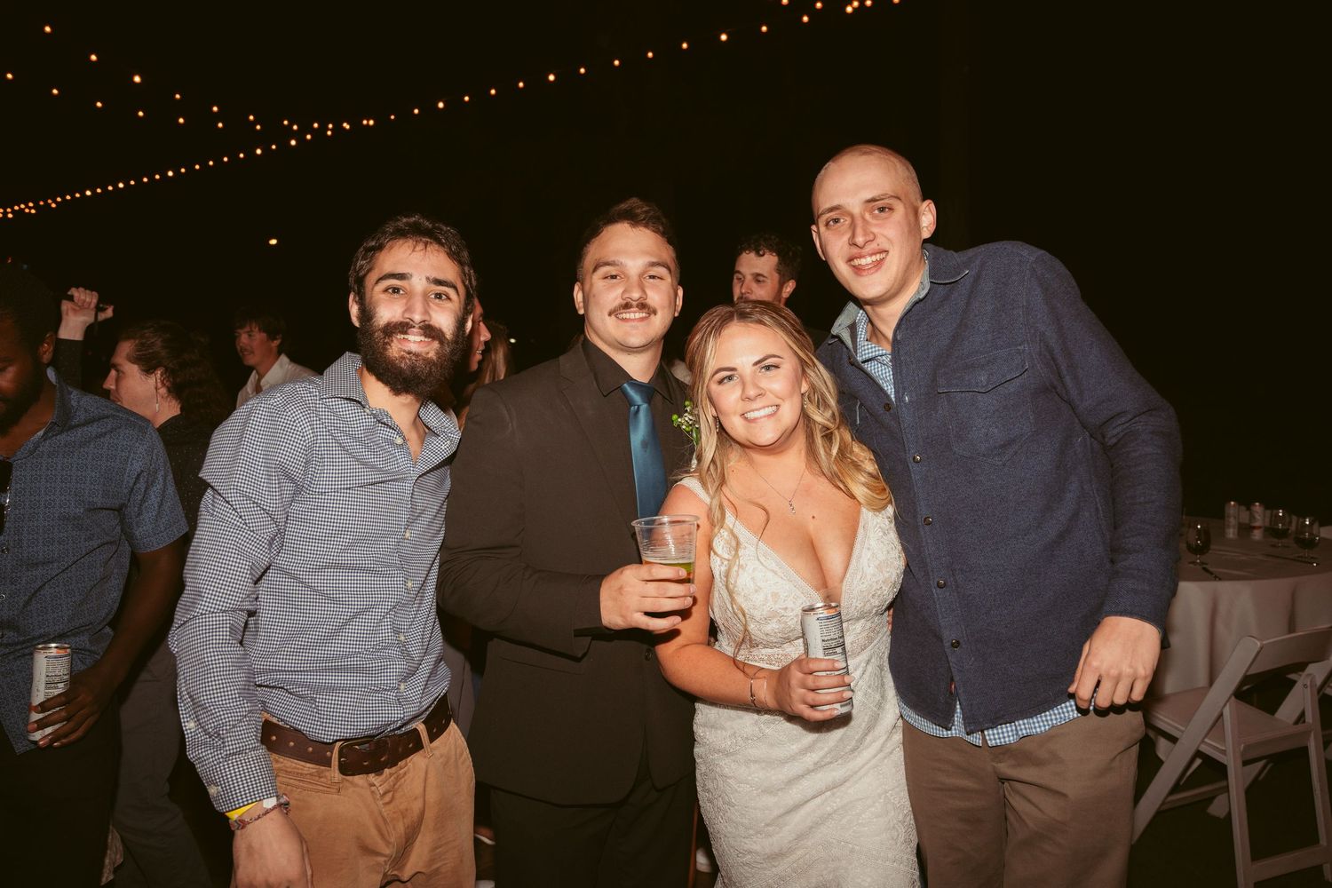 A group poses together at an outdoor evening celebration with string lights overhead.