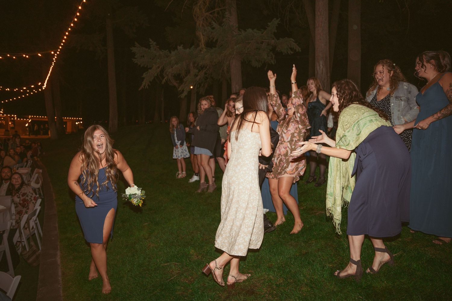 Wedding celebration on a lawn with guests dancing under outdoor string lights.