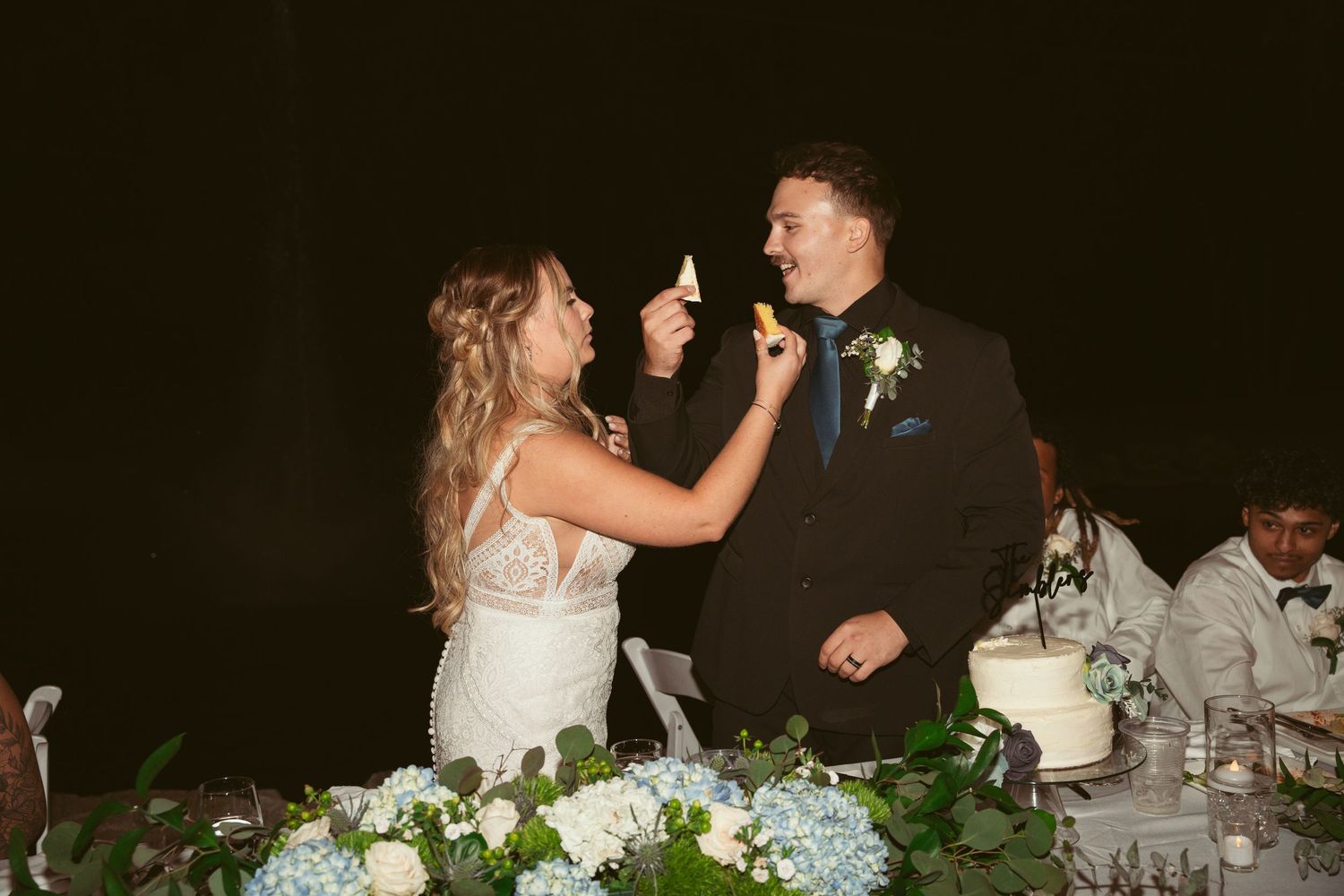 Wedding guests dance and celebrate at an outdoor evening reception under string lights.