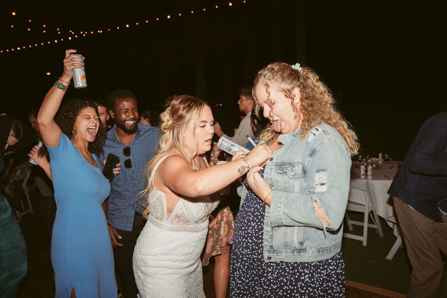People dancing together at a nighttime outdoor party with string lights overhead.