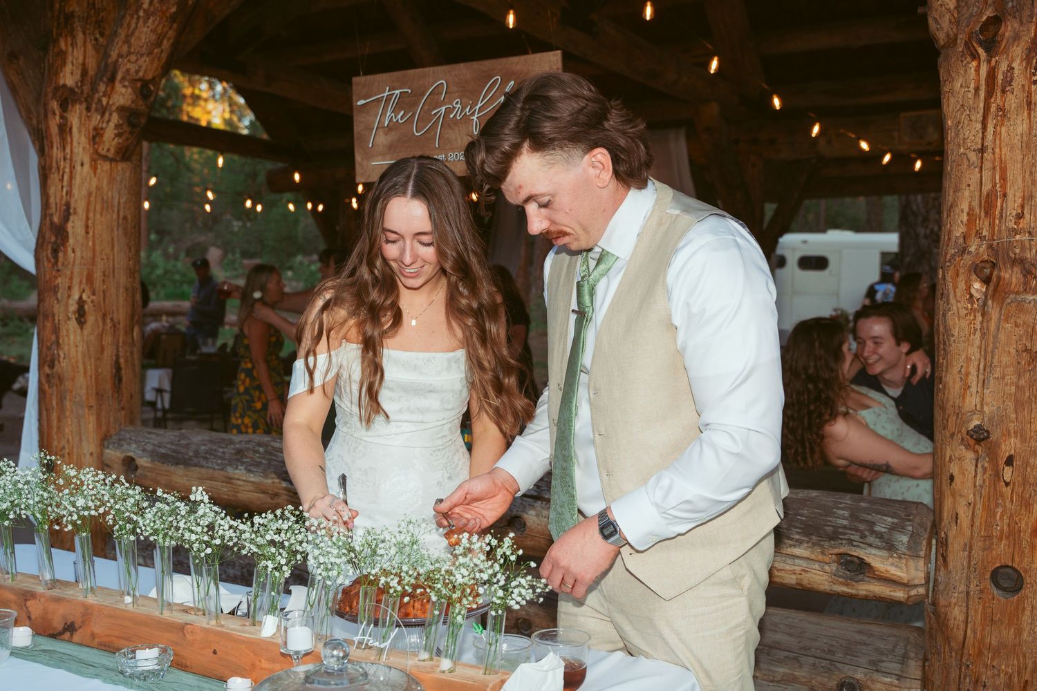 A candid reception moment at a rustic wooden venue decorated with string lights and floral arrangements.