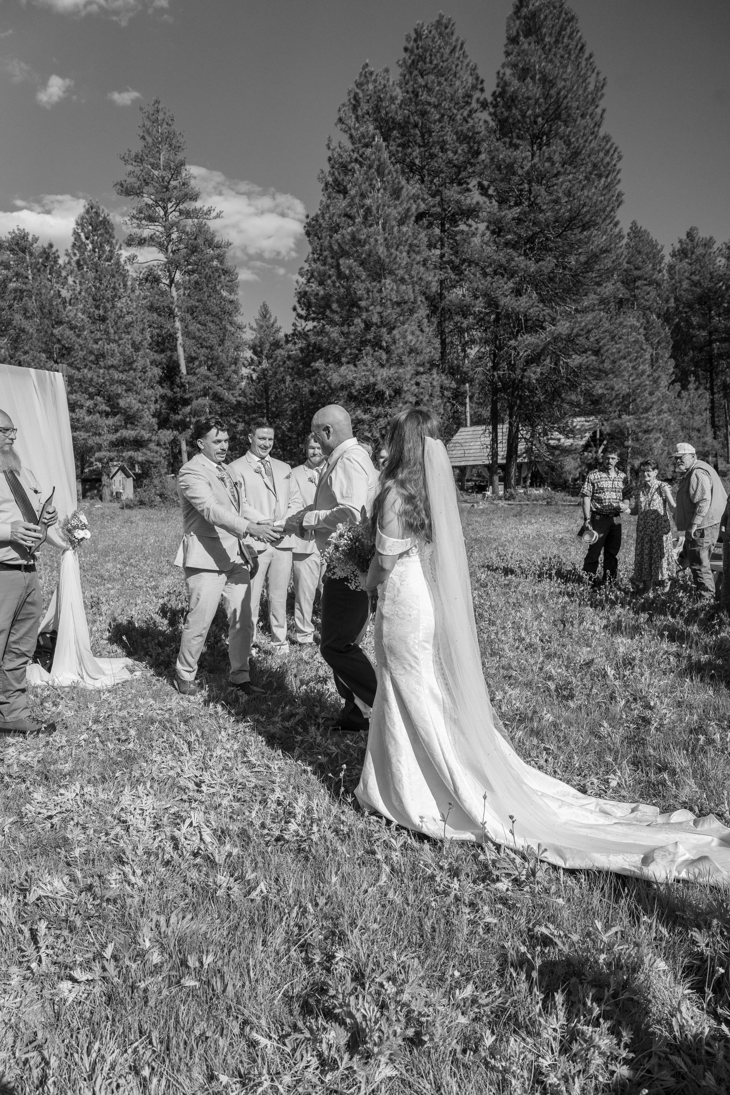 Black and white wedding ceremony photo with guests gathered in mountain meadow.