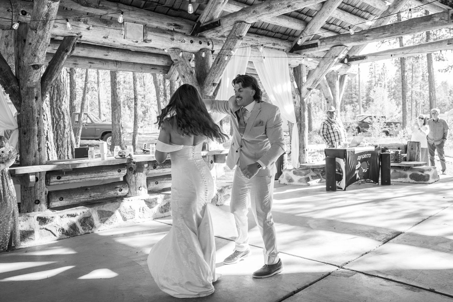 Wedding celebration dance captured in a rustic outdoor pavilion with natural lighting.