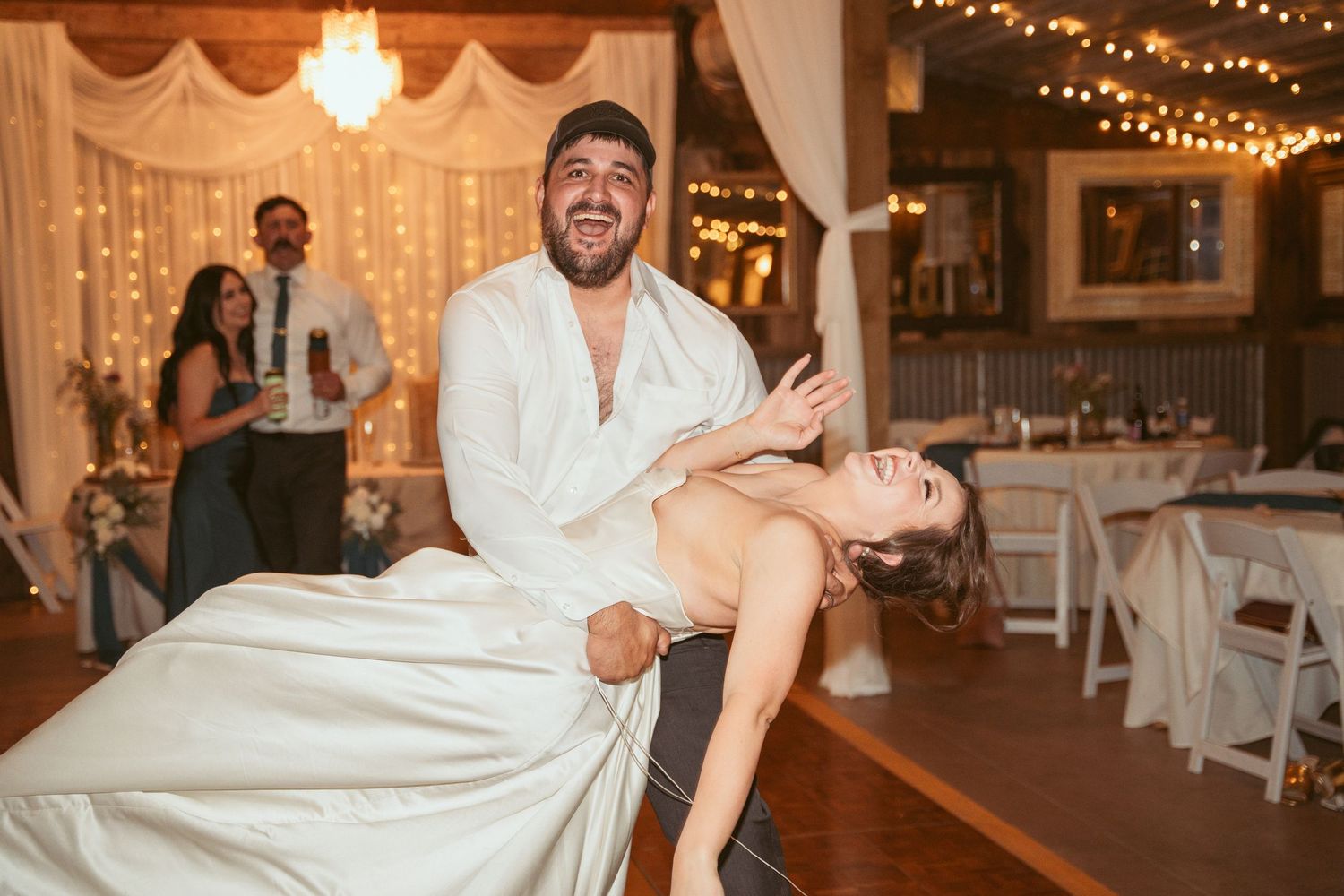Dancing couple in formal wear performing dramatic dip move on wedding reception dance floor.