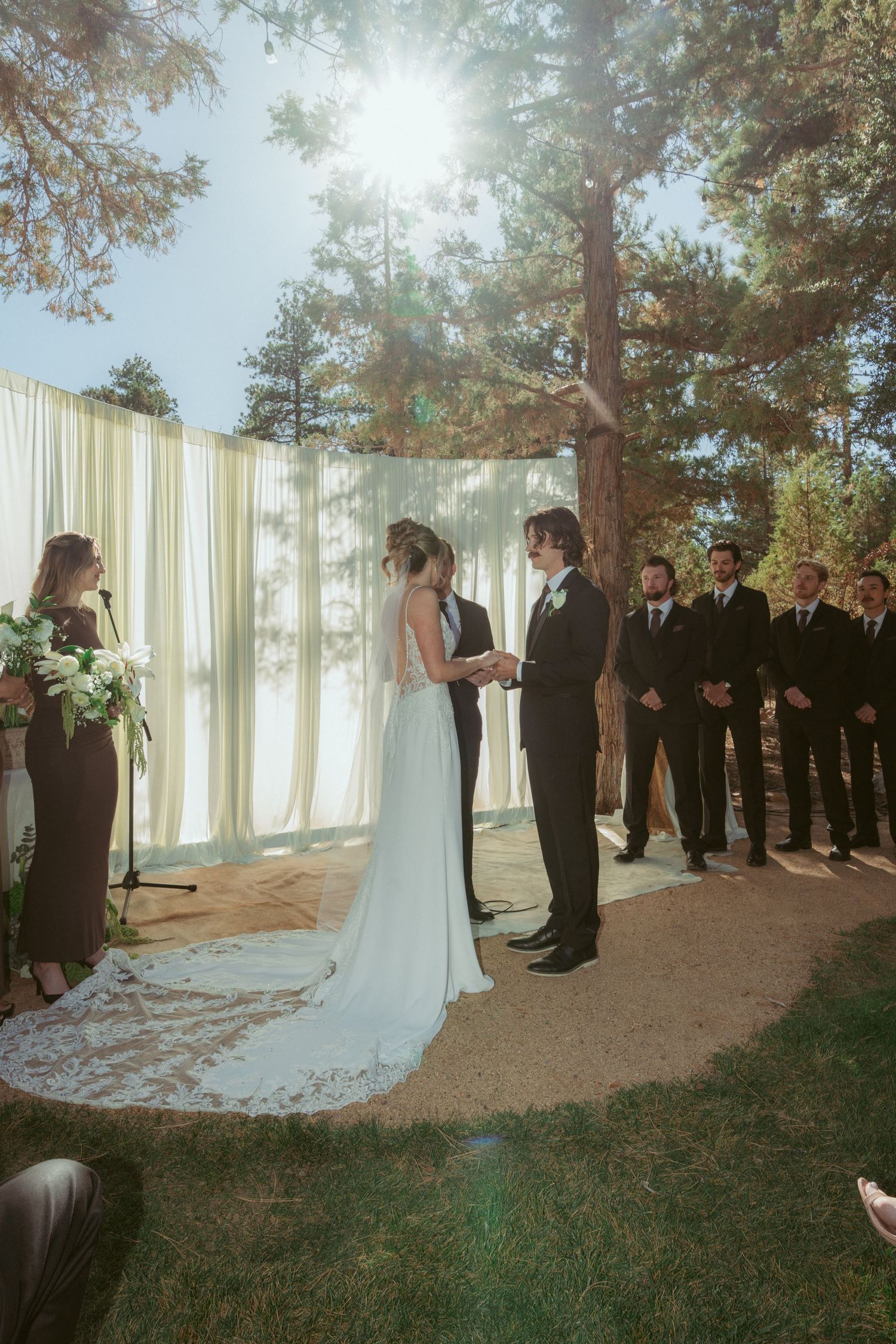 Forest wedding ceremony with sunlight streaming through trees and white curtain backdrop.