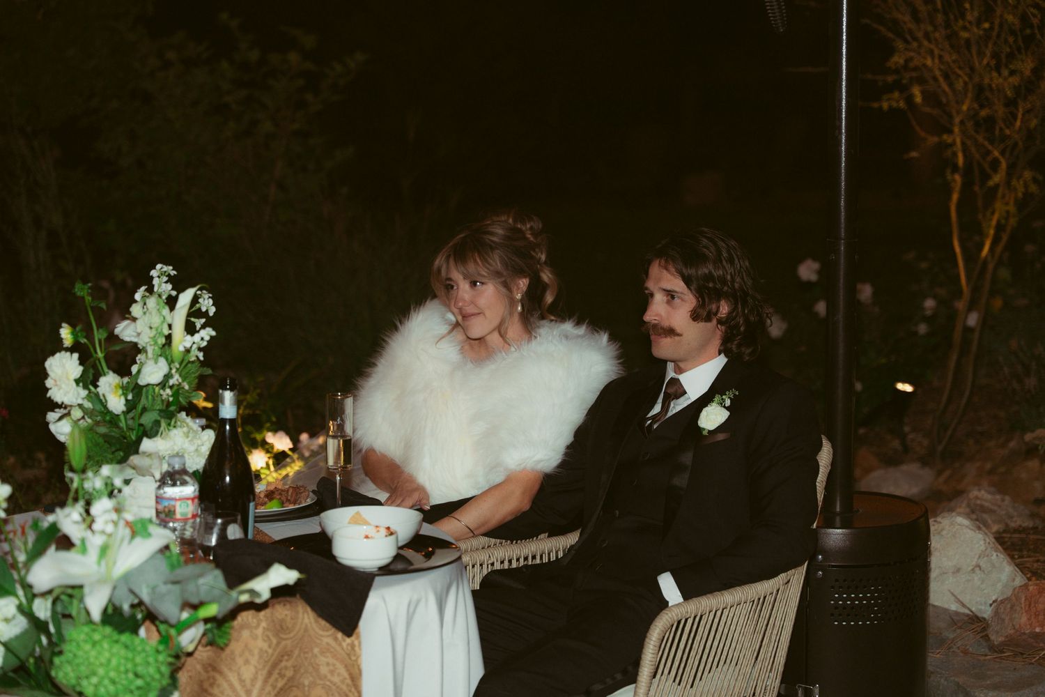 Outdoor wedding celebration at night with dancing and festive lighting.