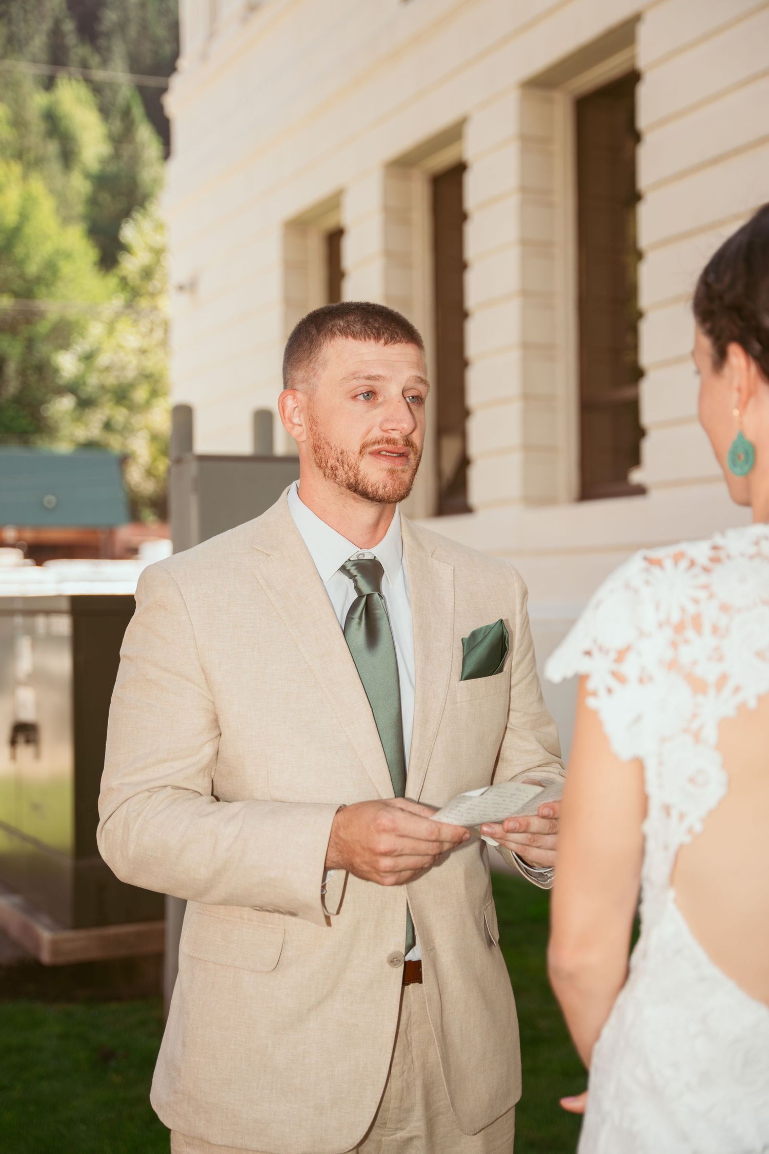 A couple shares handwritten letters during their wedding ceremony outside a white building.