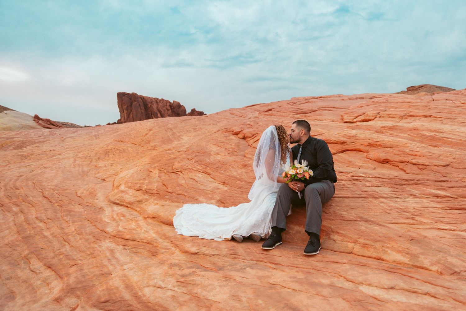 Wedding couple embraces on smooth red rock formations in a desert setting.