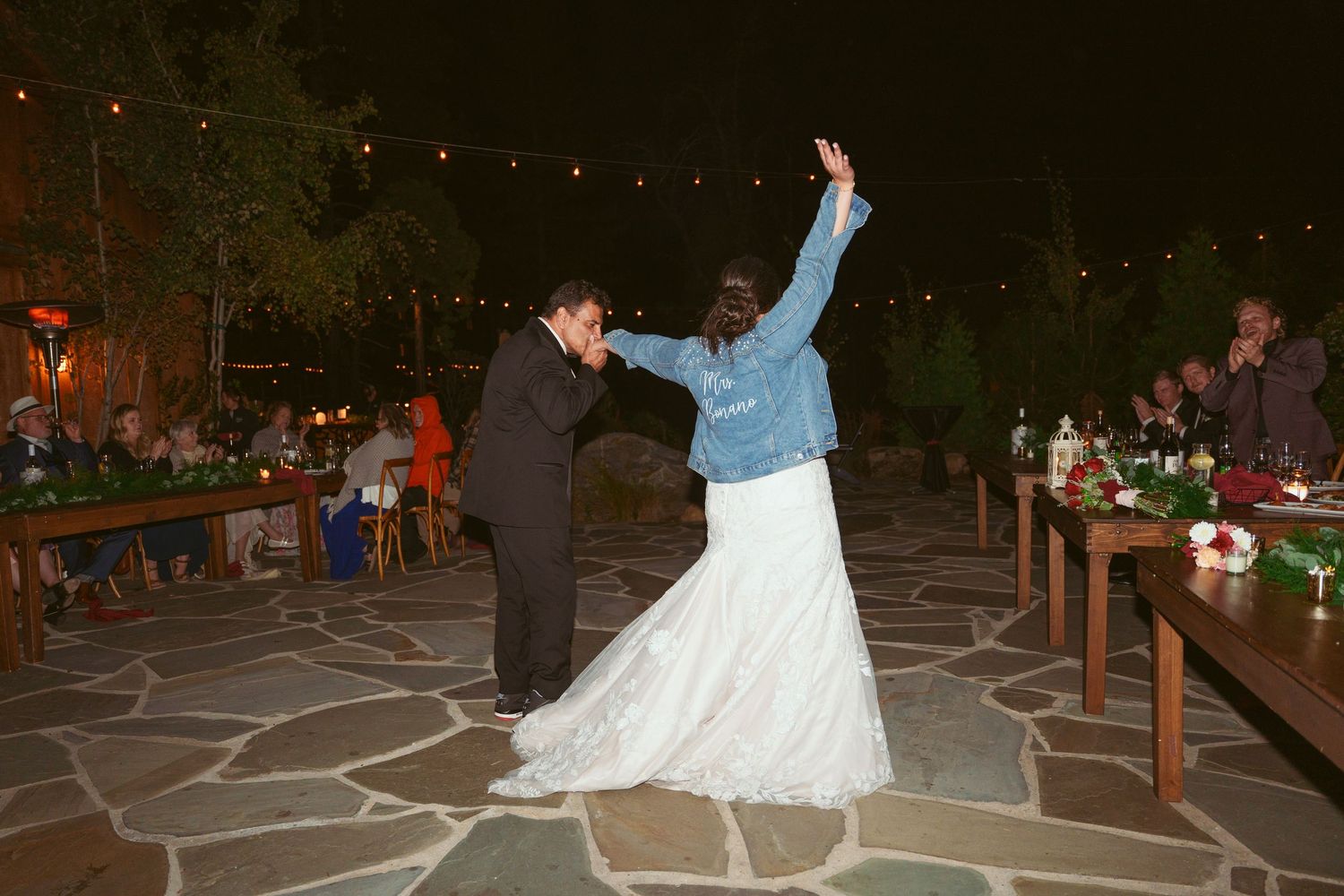 A couple dances on a stone patio during their wedding reception at dusk.