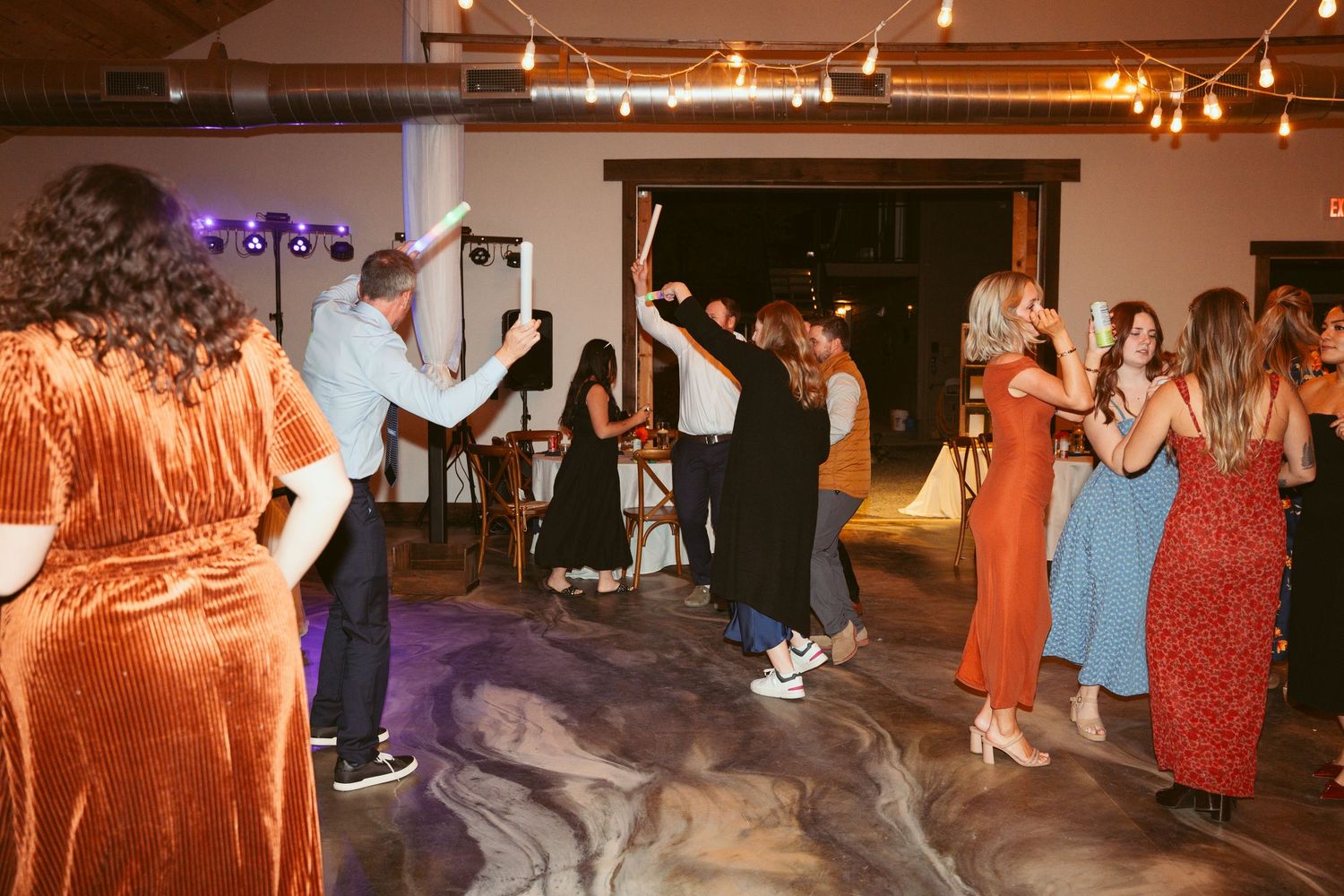 Wedding reception dance floor filled with guests celebrating under warm string lights.