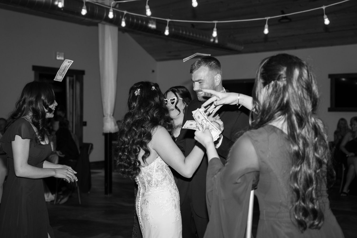 Wedding reception guests dancing energetically on a wooden dance floor under string lights.