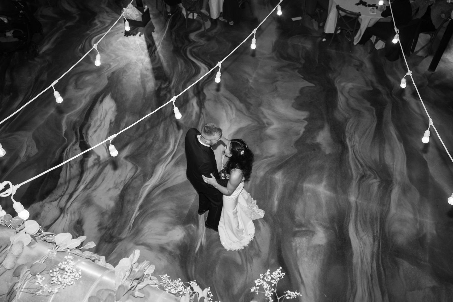 Black and white photo of a wedding dance with string lights creating a dreamy atmosphere.