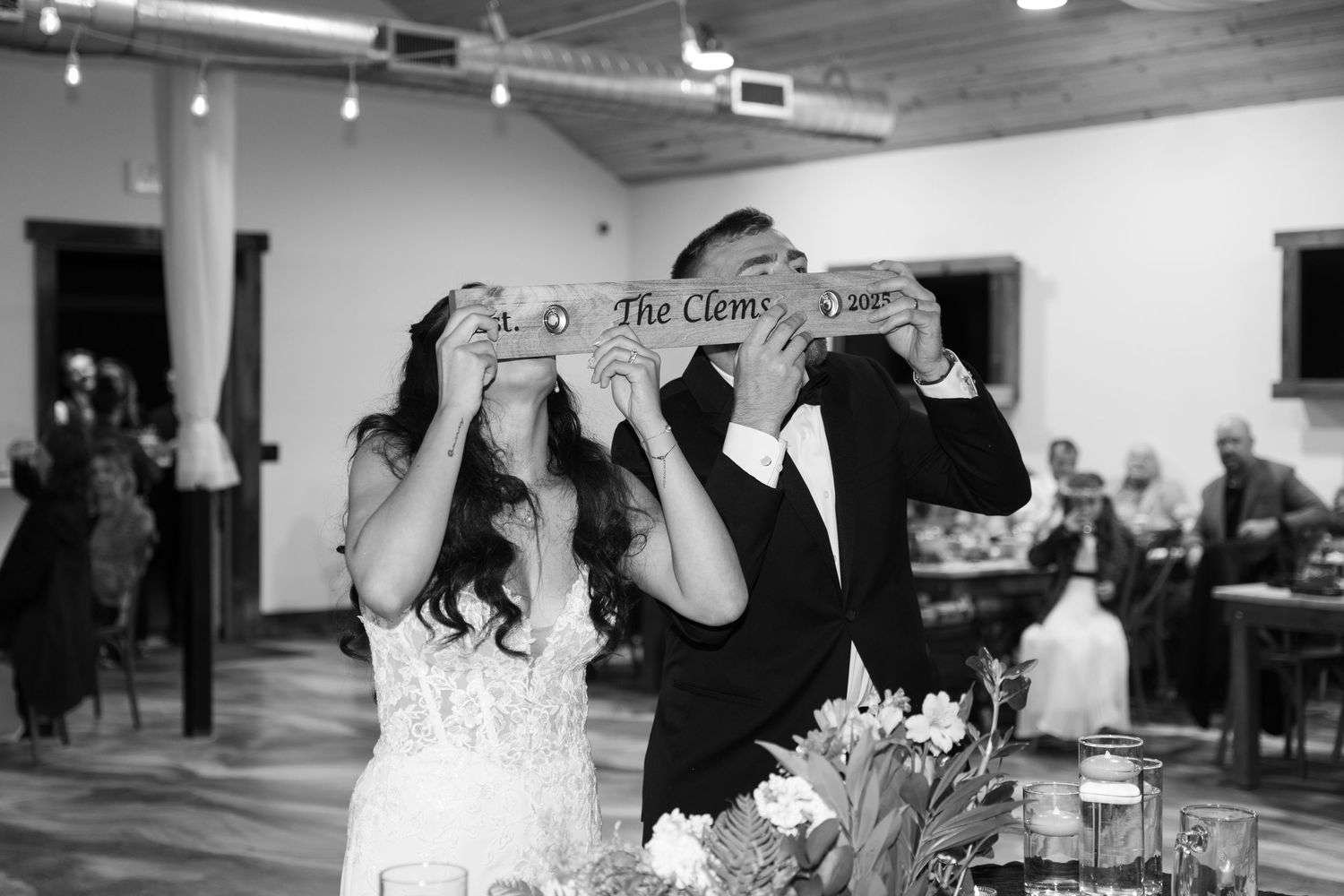 Black and white photo of wedding reception celebration with guests gathered in an indoor venue.