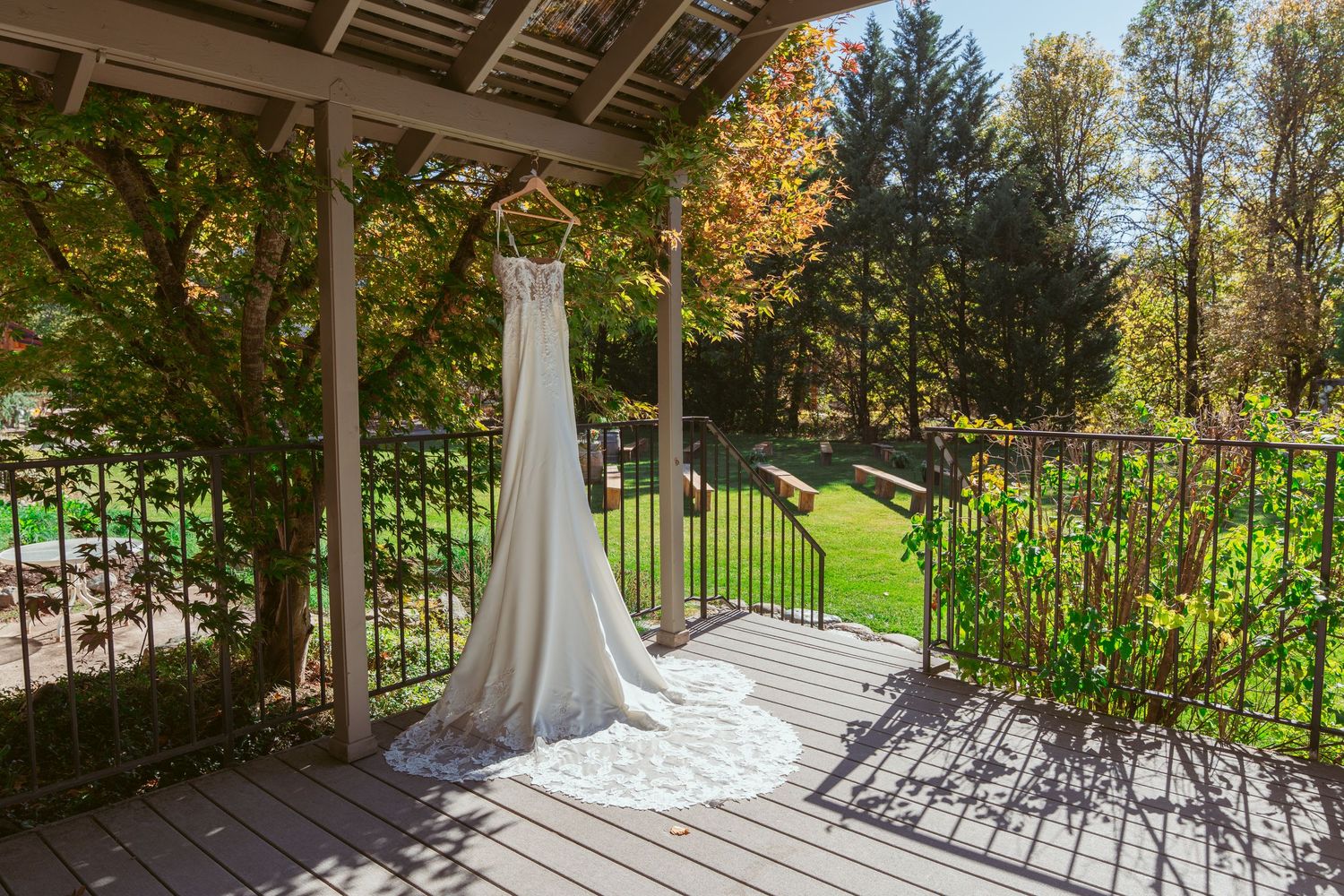 Elegant white wedding dress hanging on a covered porch with autumn trees in the background.