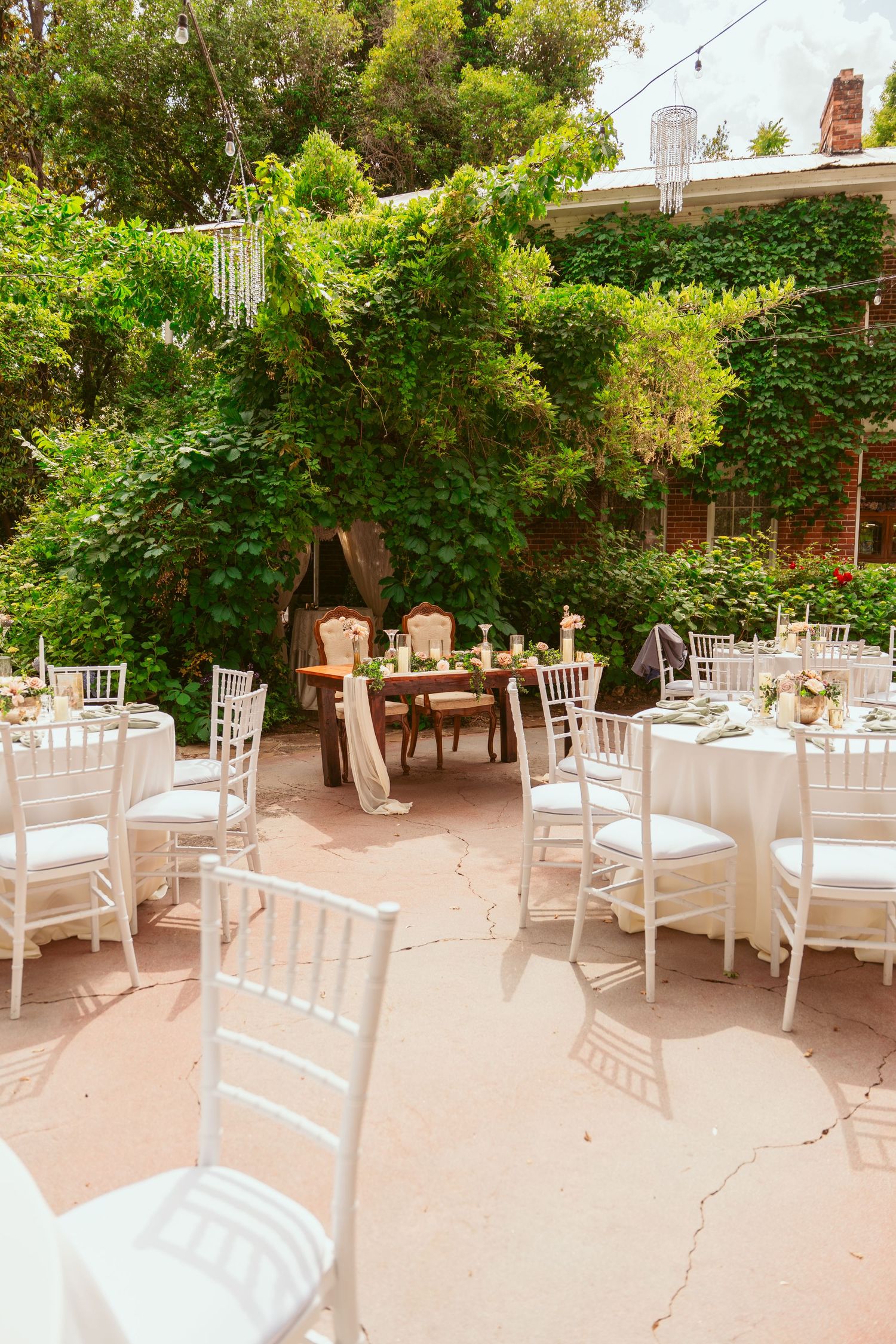 White chairs arranged in rows for an outdoor garden wedding ceremony under green trees and natural lighting.