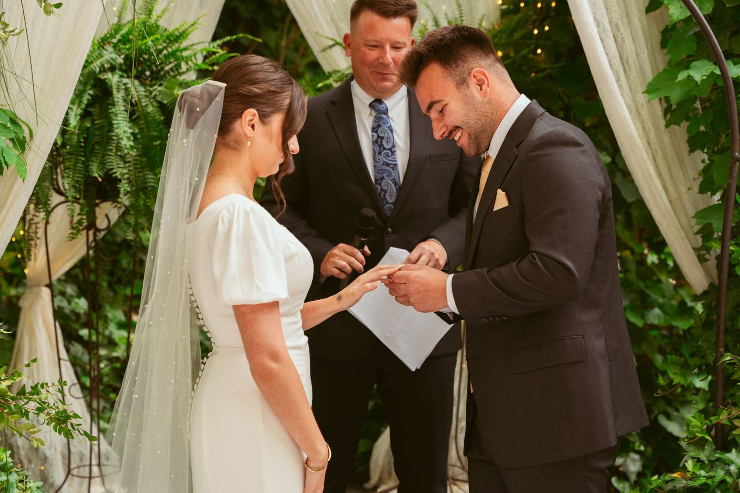 Wedding ceremony under a floral arch with couple exchanging rings.