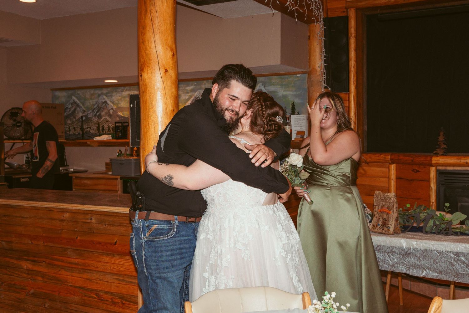 Wedding guests embrace and share emotional moments during a reception in a rustic wooden venue.