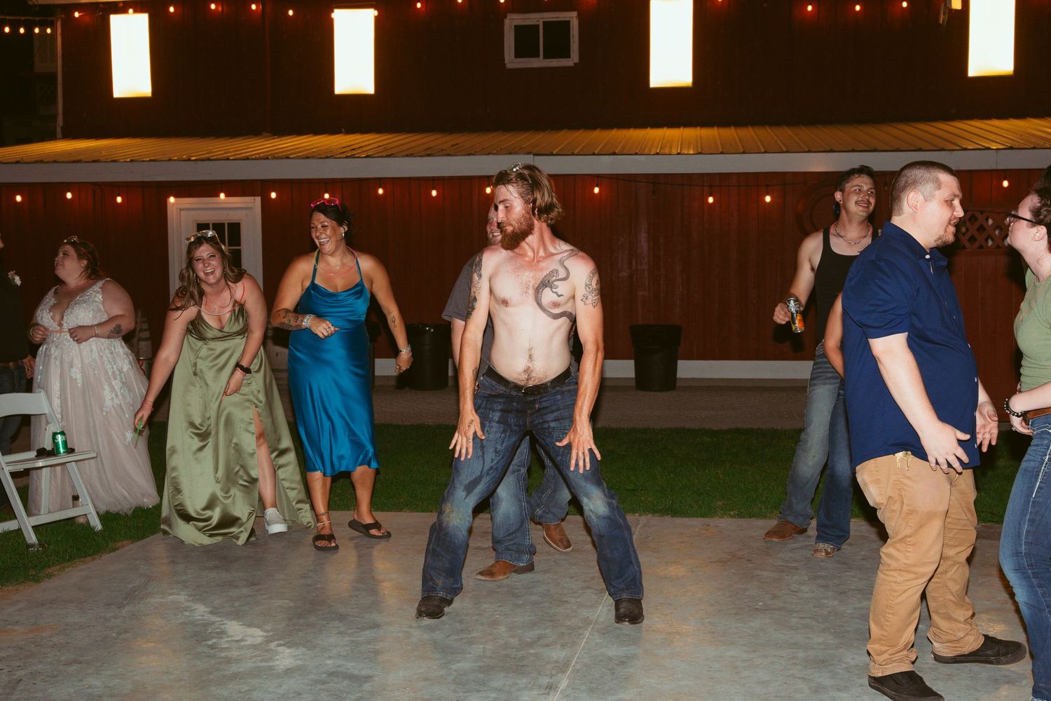Wedding guests dance under string lights at an outdoor evening reception.