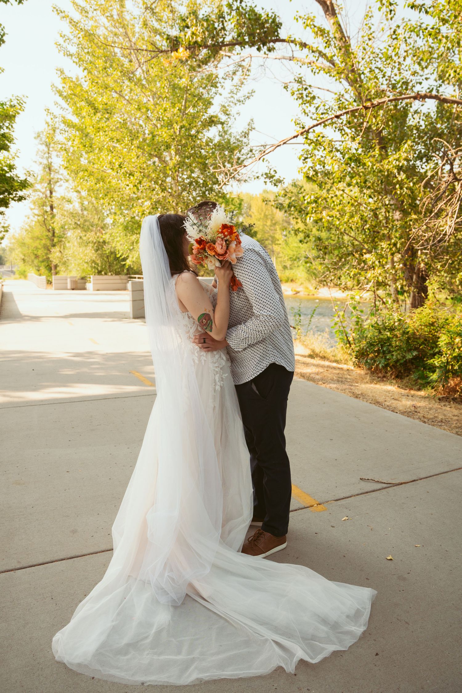 Newlyweds embrace on a sunlit pathway with golden leaves in the background.