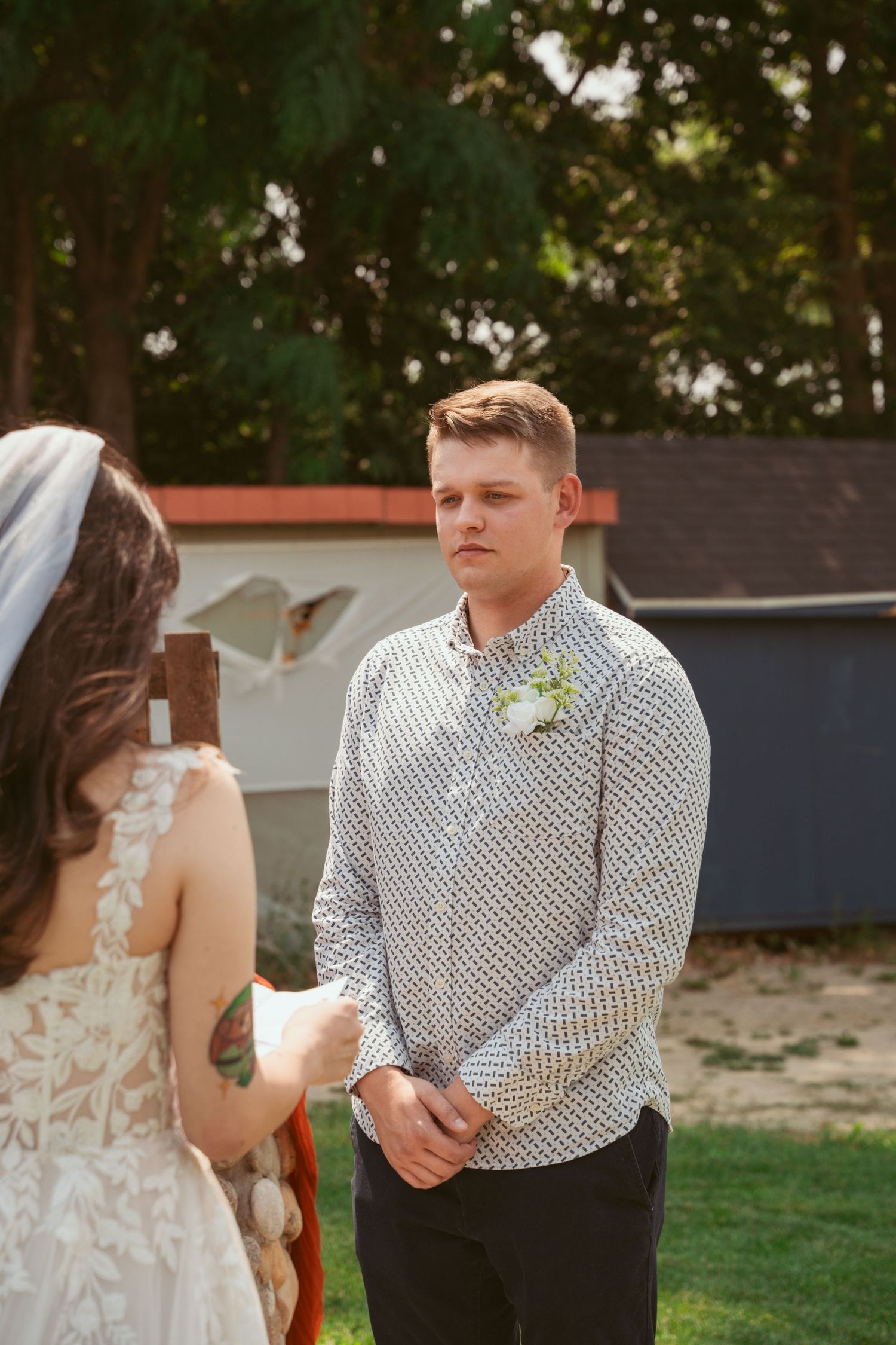 A couple stands together during an outdoor ceremony with greenery in the background.