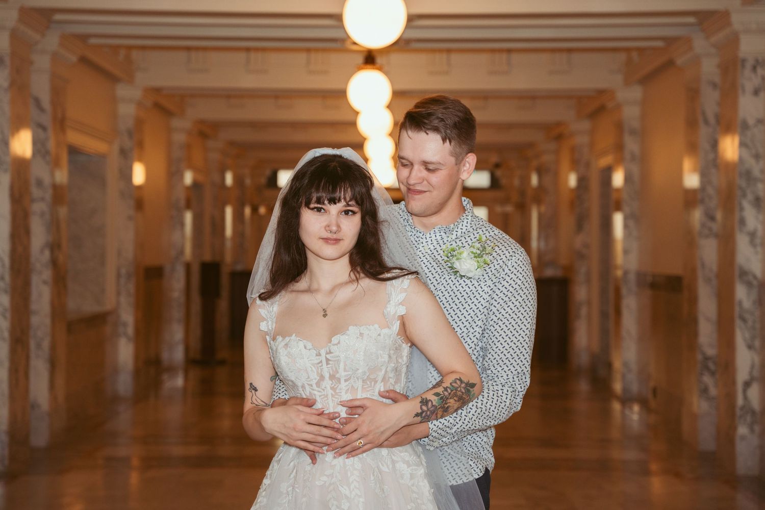 Couple dancing in an elegant columned hallway with warm lighting.
