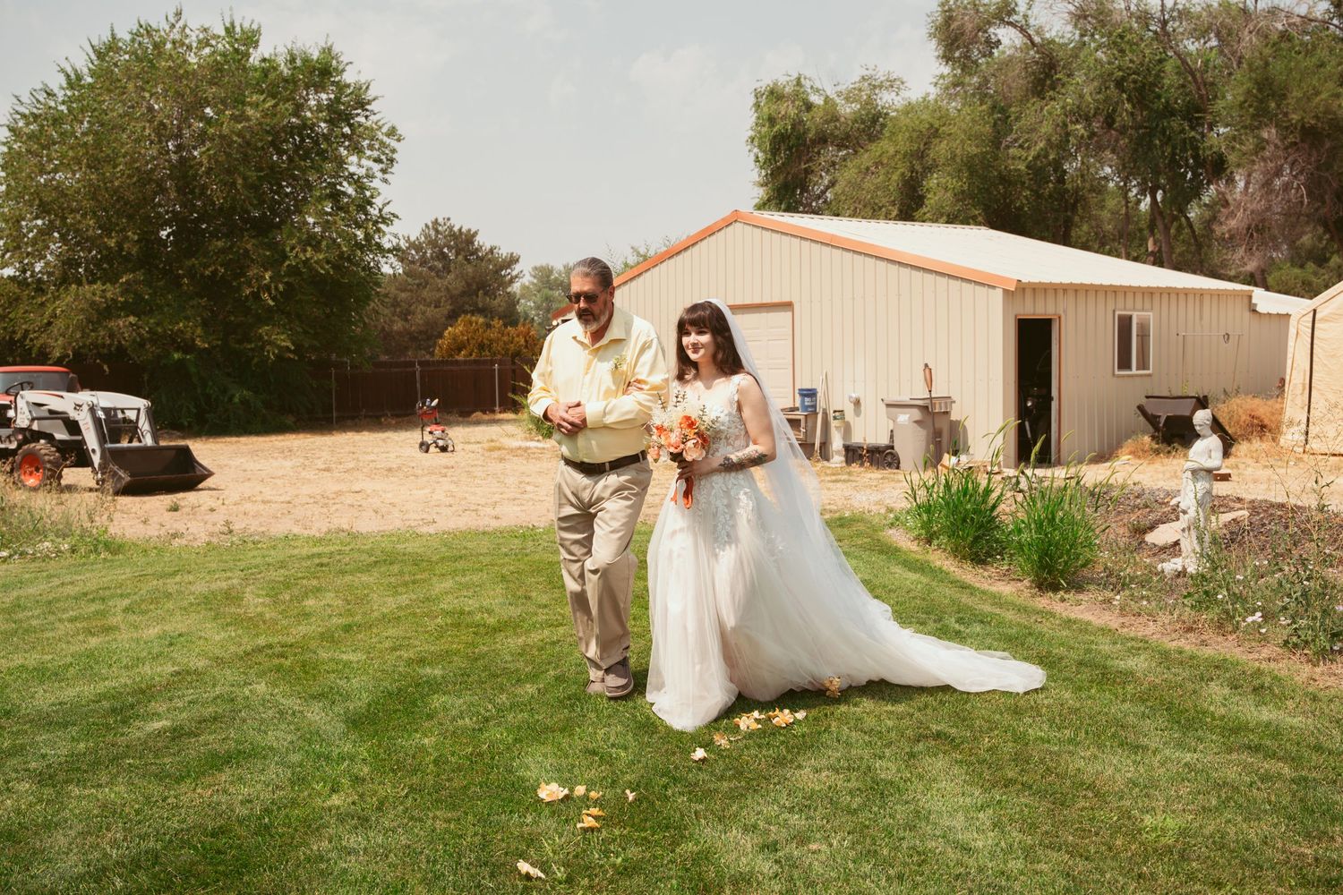 Panoramic view of an outdoor wedding venue with green lawn and rustic buildings.