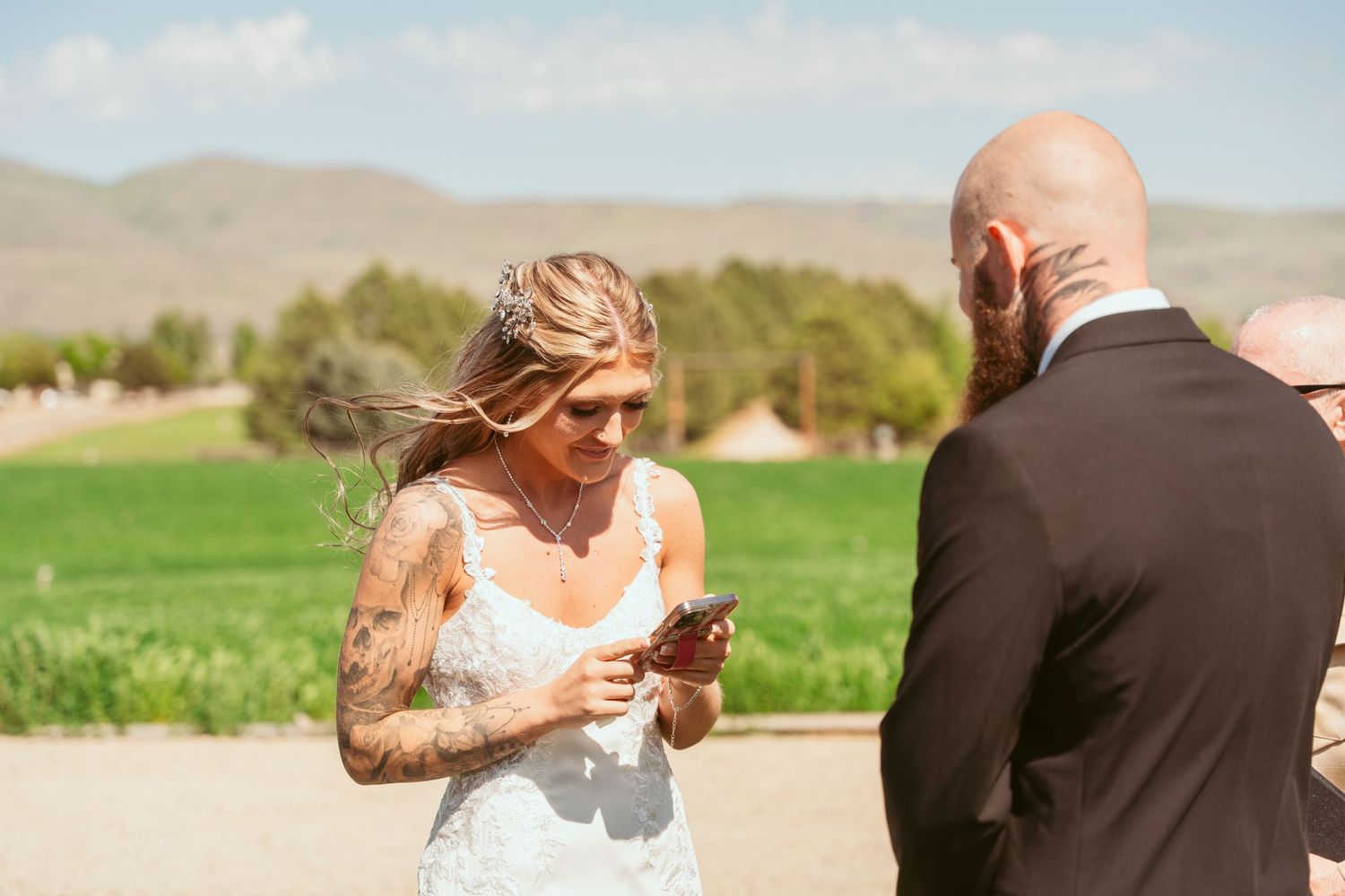 Wedding ceremony exchange on grassy field with mountains in distance.