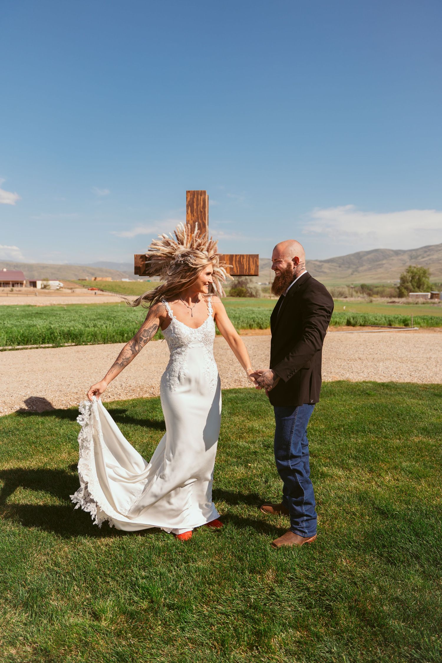 Playful wedding photo sequence in an outdoor field with wooden cross and mountains.