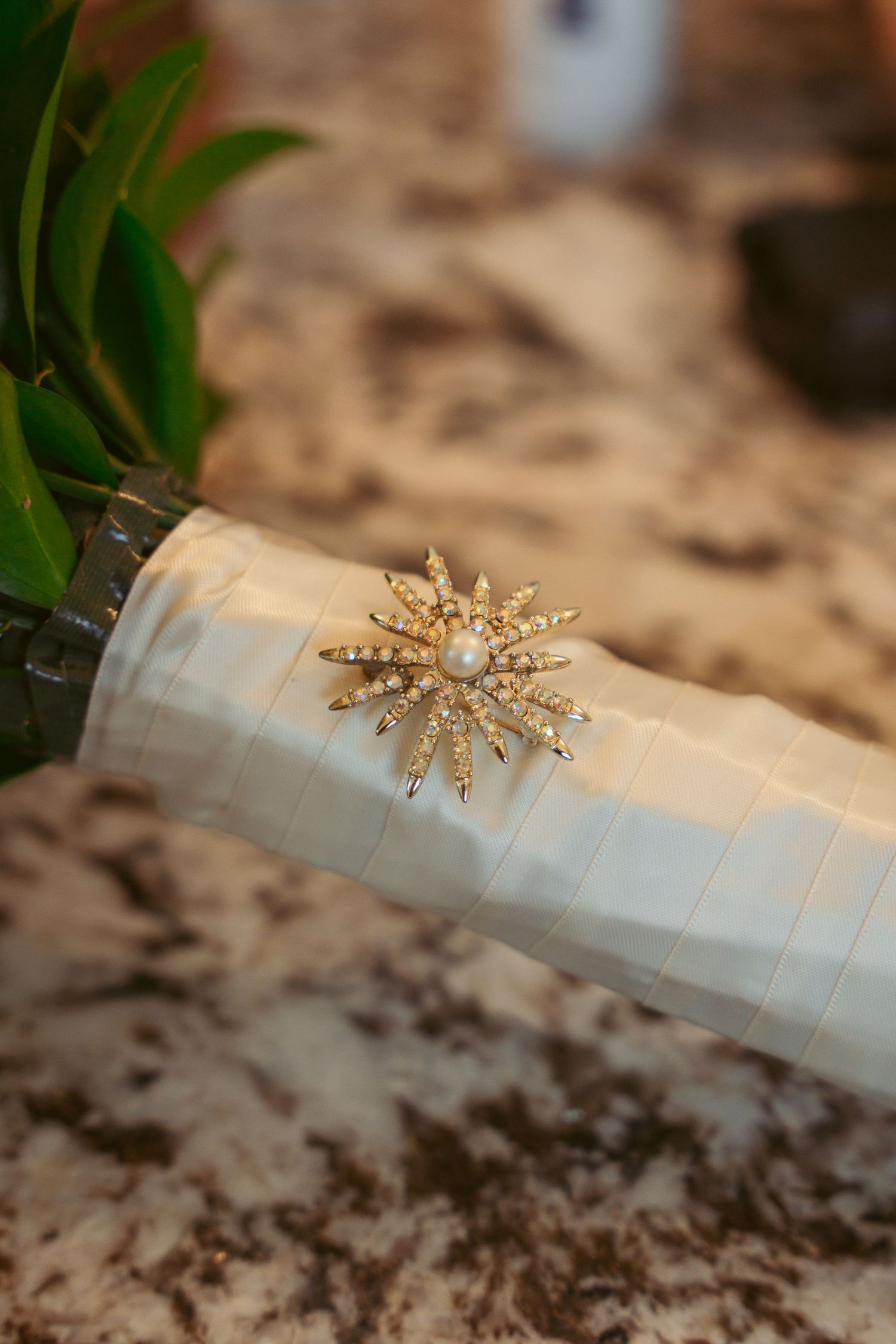 Decorative gold starburst brooch or pin displayed on white fabric with green foliage.