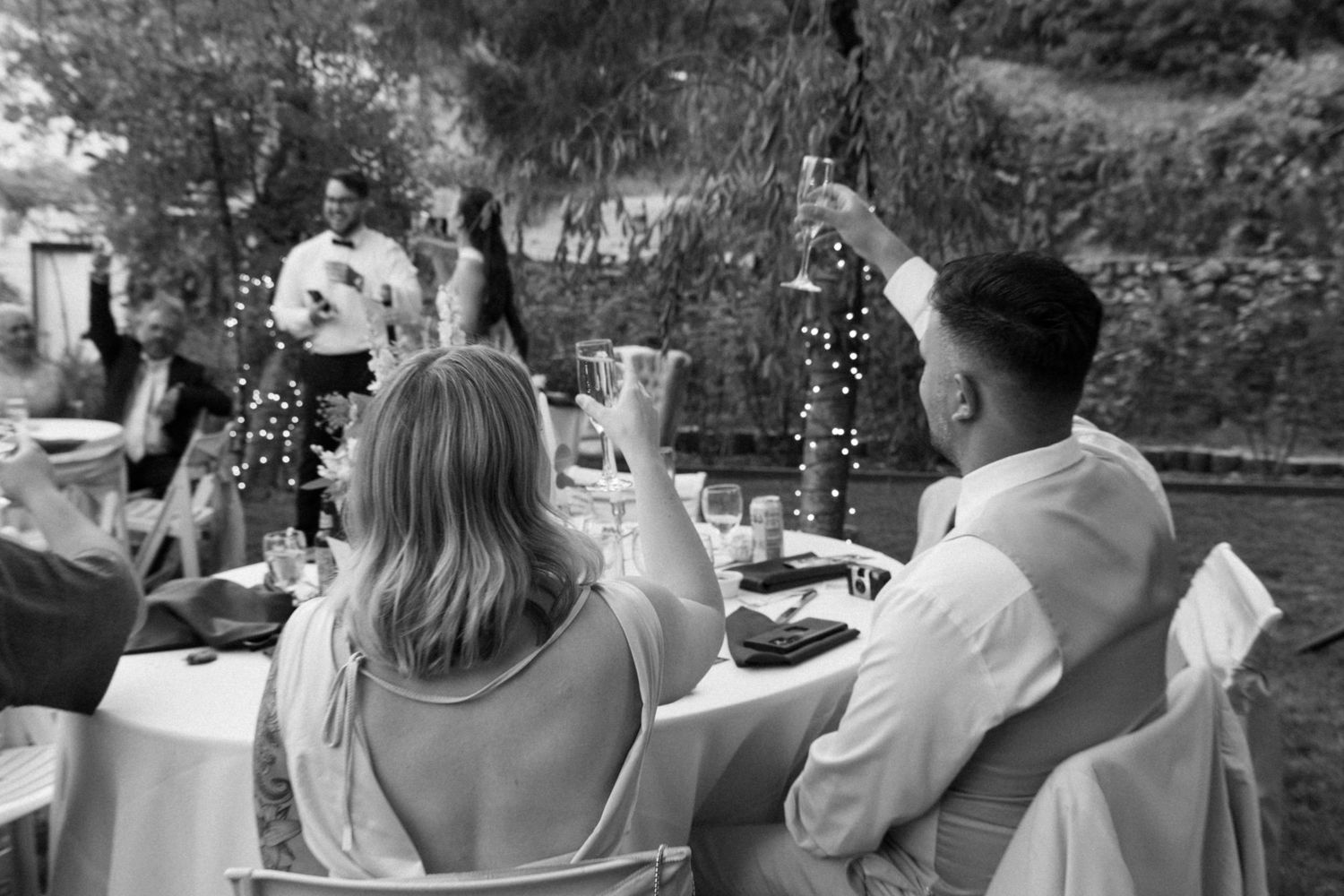 Black and white panoramic collage showing candid moments at an outdoor wedding celebration.