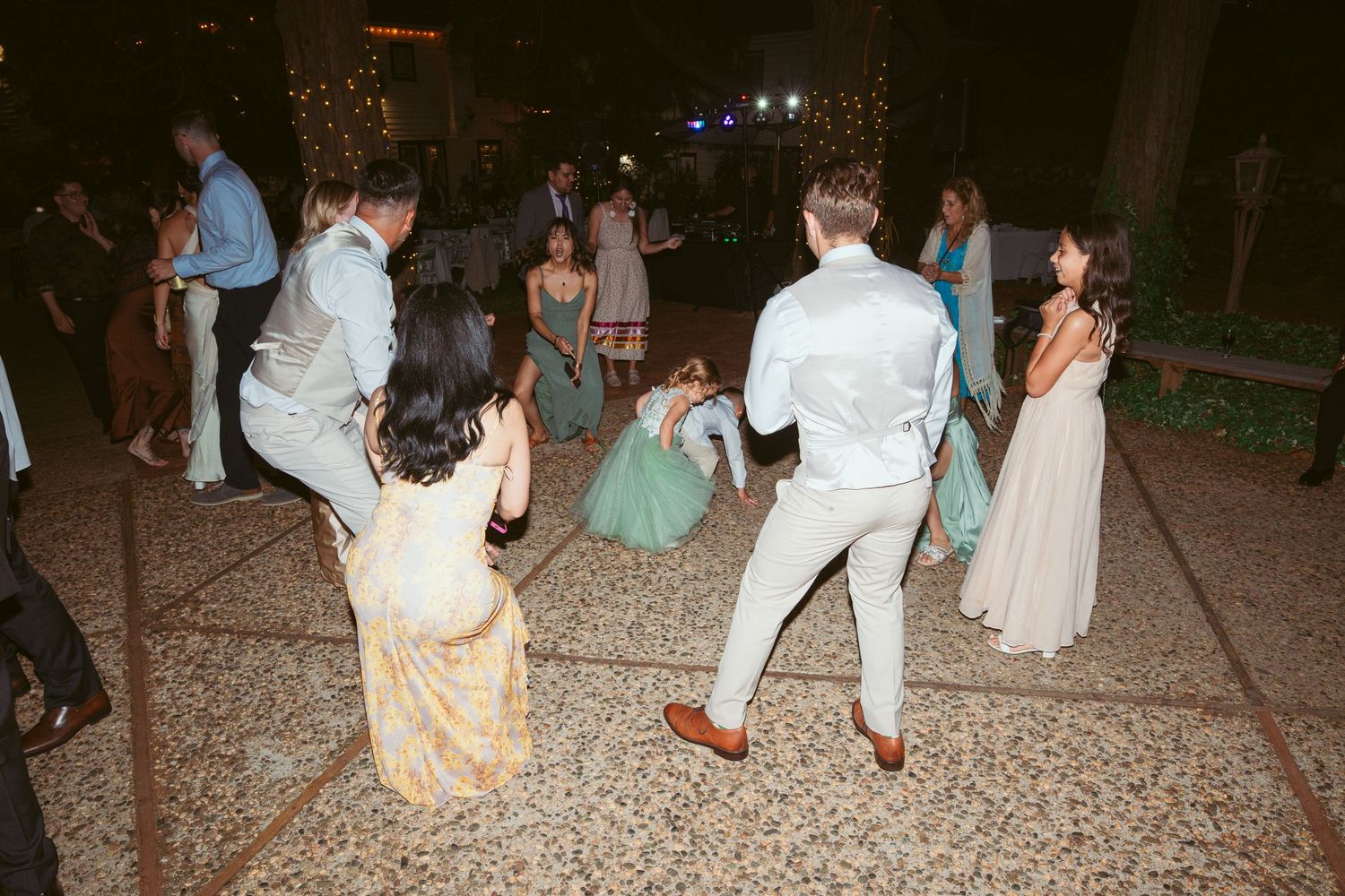 Wedding guests dancing on stone patio during evening outdoor reception.