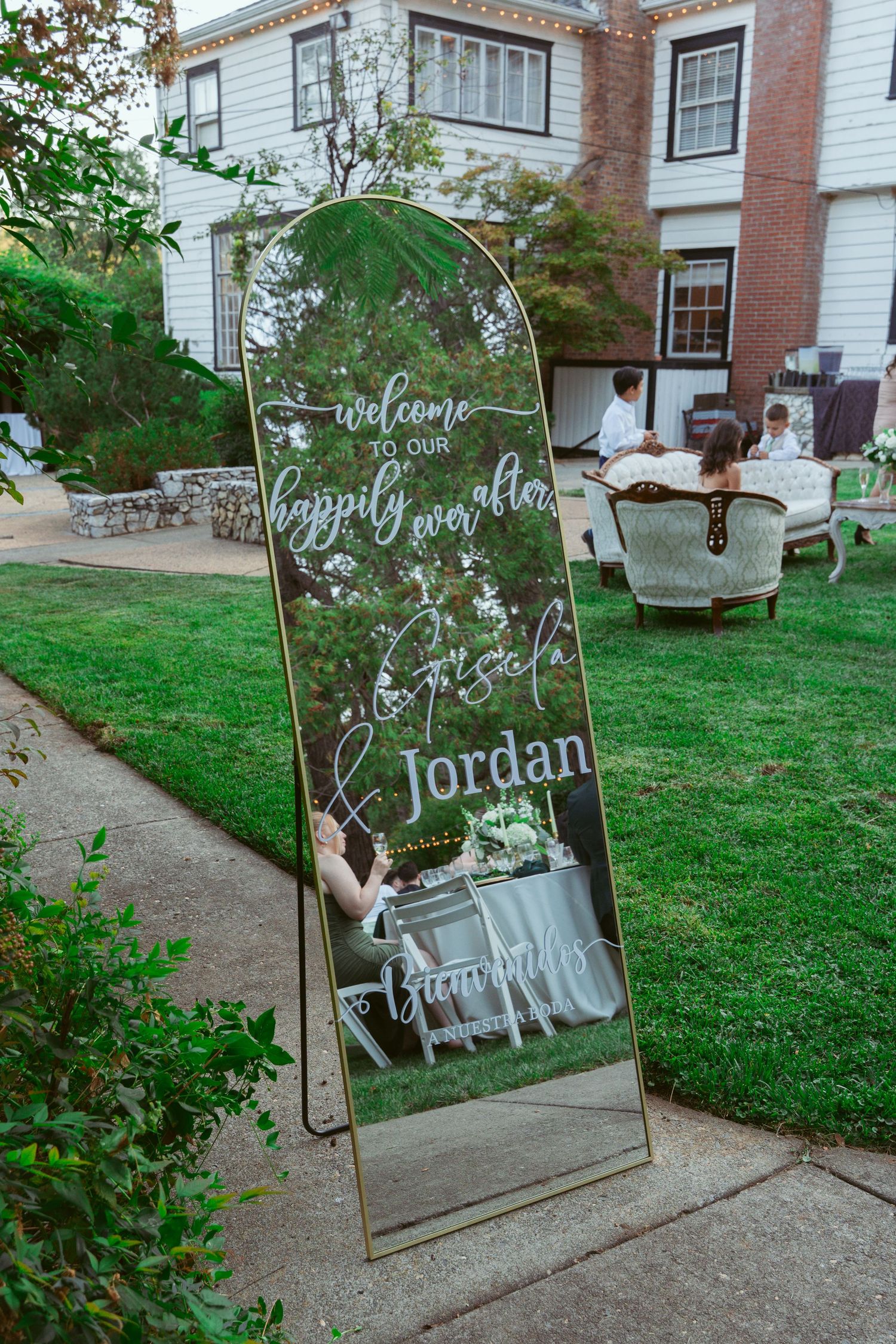 Decorative mirror wedding welcome sign with calligraphy displayed in a garden setting.