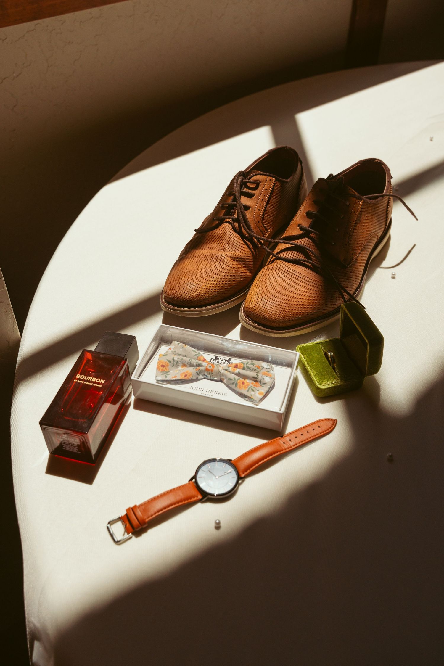 Brown leather dress shoes with accessories arranged in dramatic lighting.