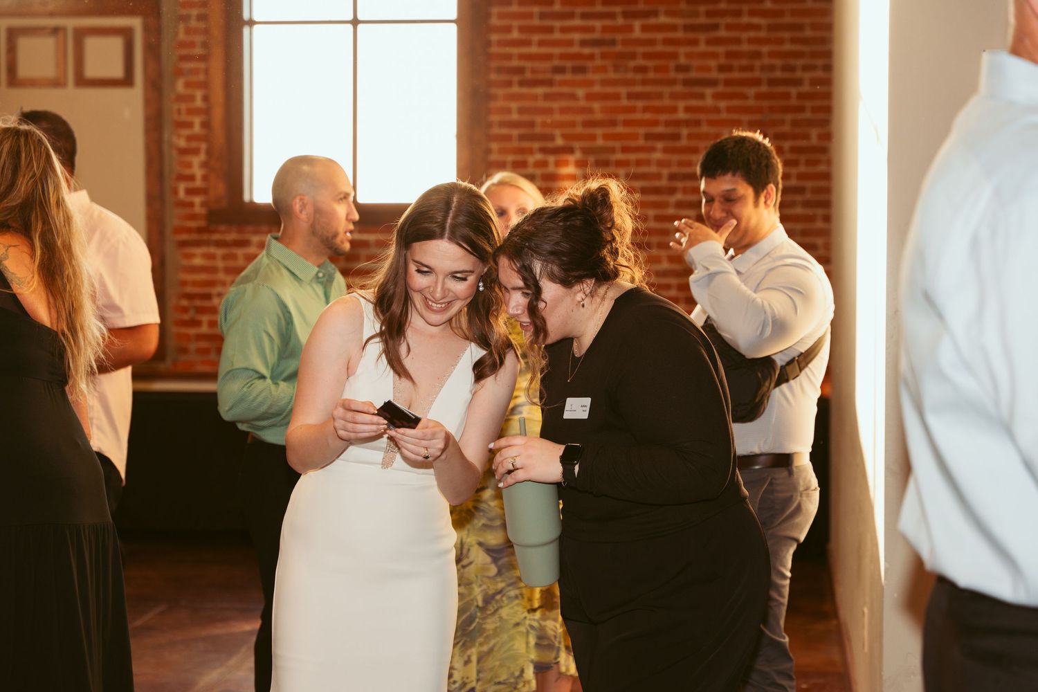 Guests mingling and dancing at a wedding reception in an industrial-style venue with exposed brick walls.