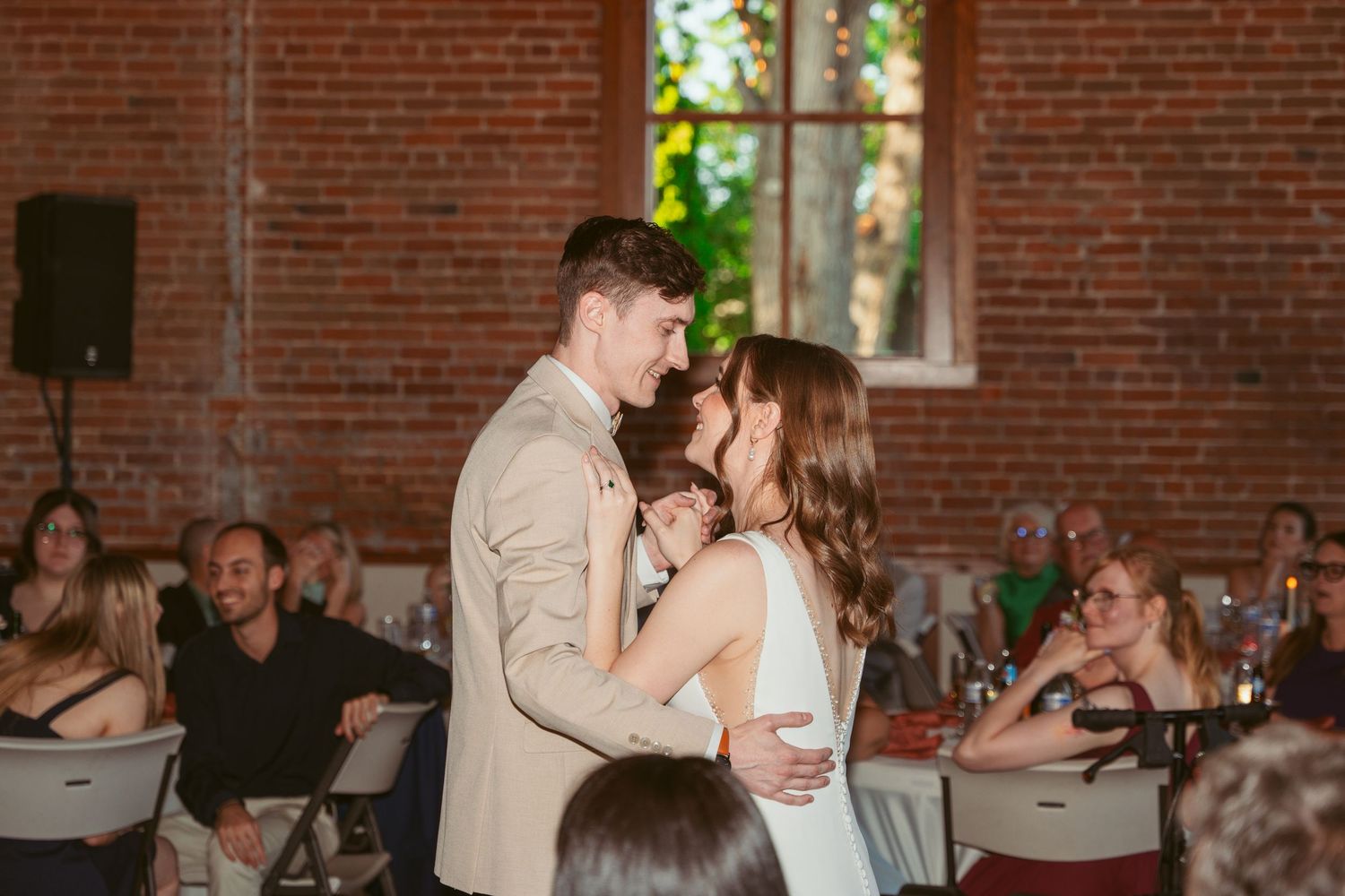 Wedding celebration in brick-walled venue with natural light and seated guests.