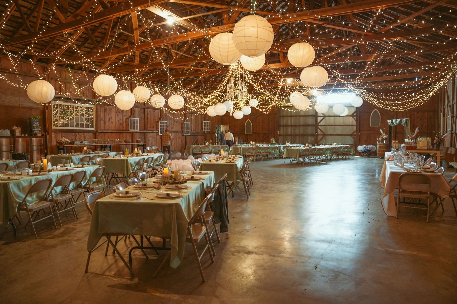 Large rustic barn venue decorated with string lights and paper lanterns creating romantic ambiance.