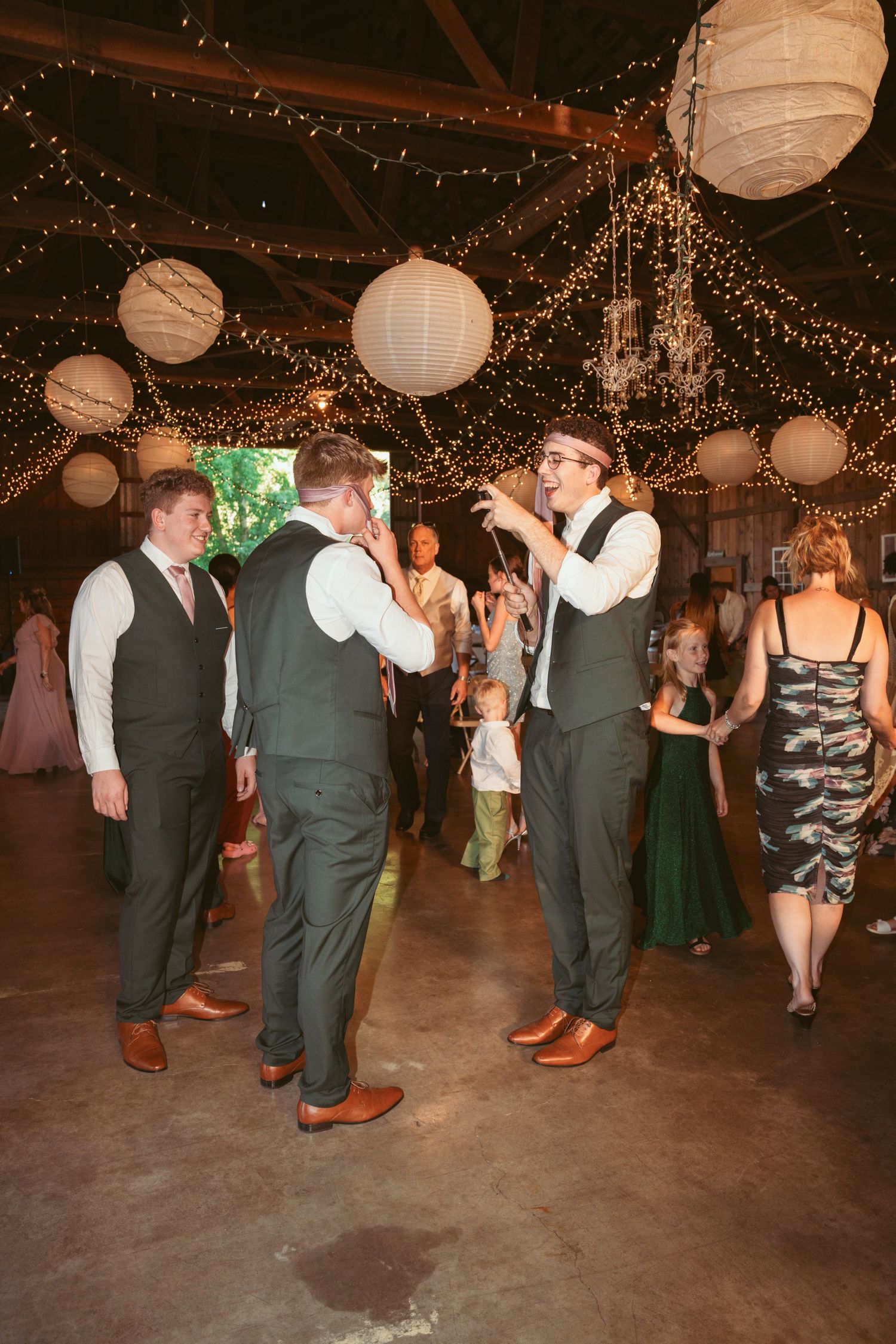 Guests dancing at a wedding reception under decorative lighting in a rustic venue.
