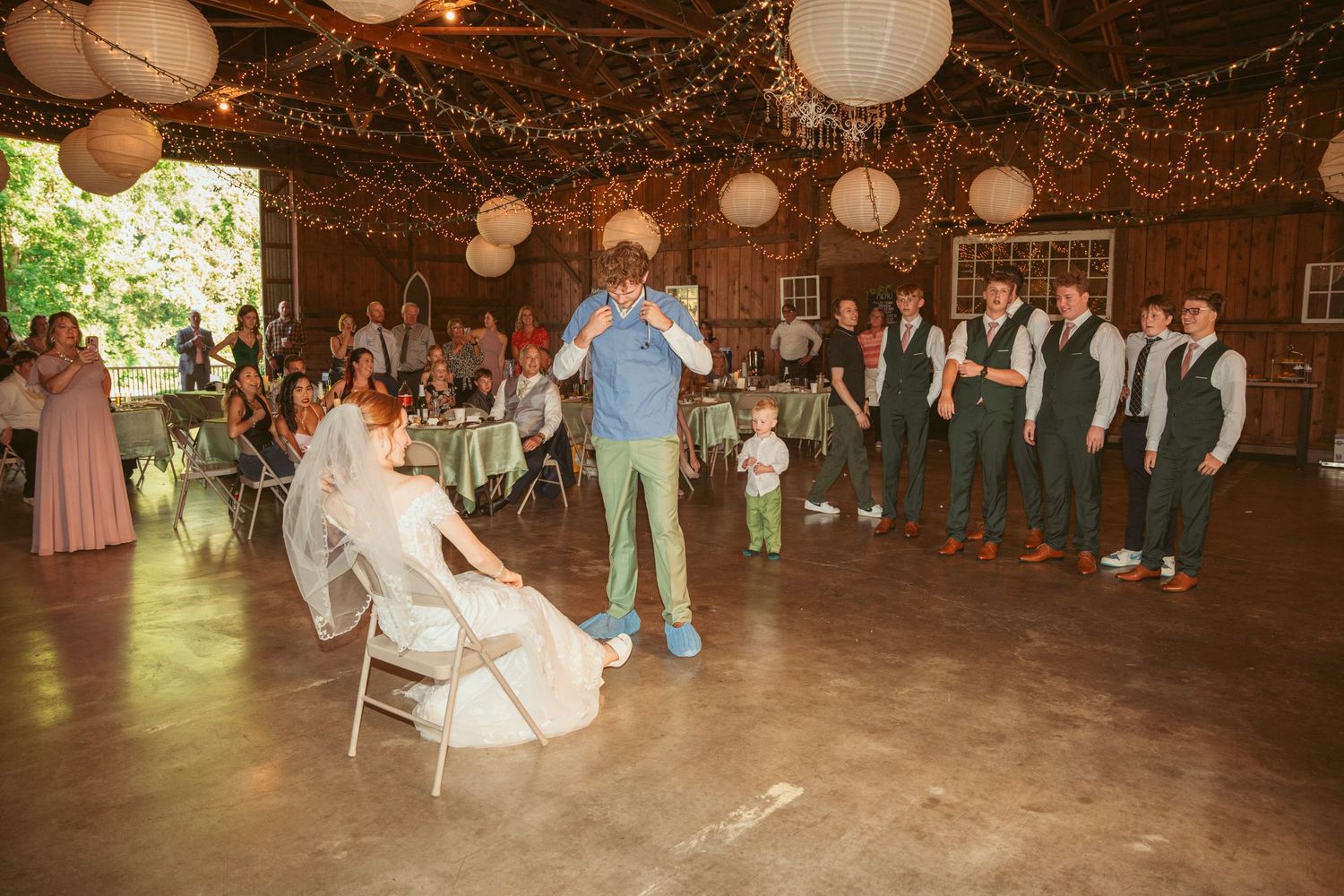 Guests gathered in a barn decorated with hanging lanterns and twinkle lights for a celebration.