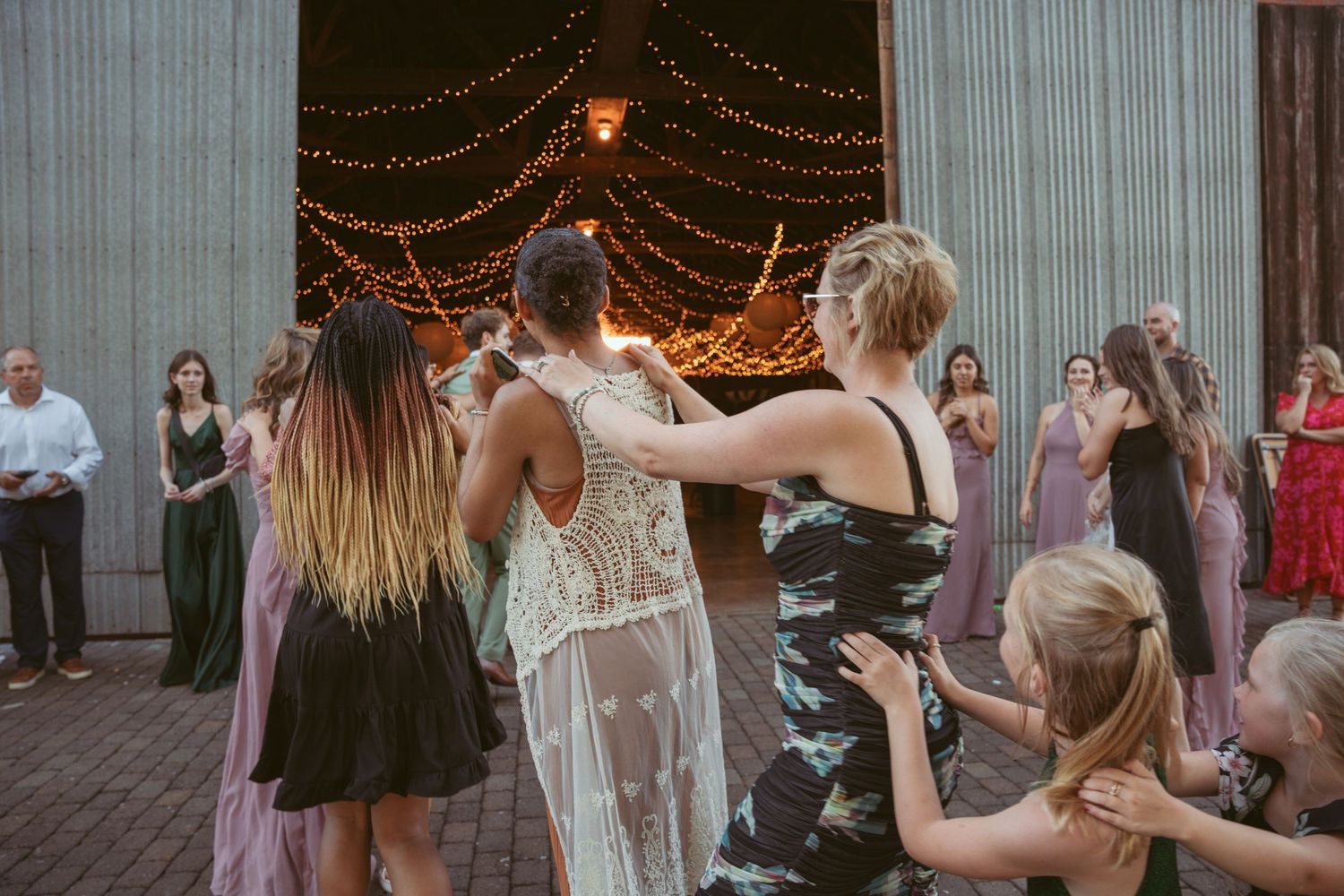 Festive group dance routine unfolds at outdoor wedding reception with twinkle light ambiance.