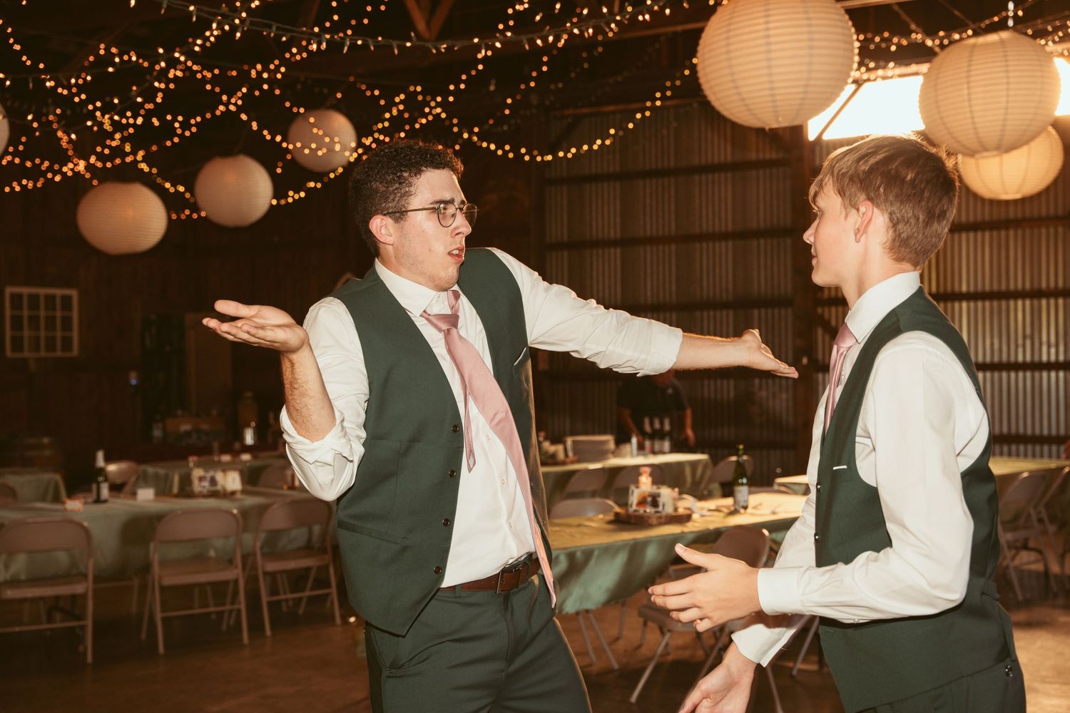 Wedding guests enjoying playful dance moments in a barn decorated with twinkling lights.