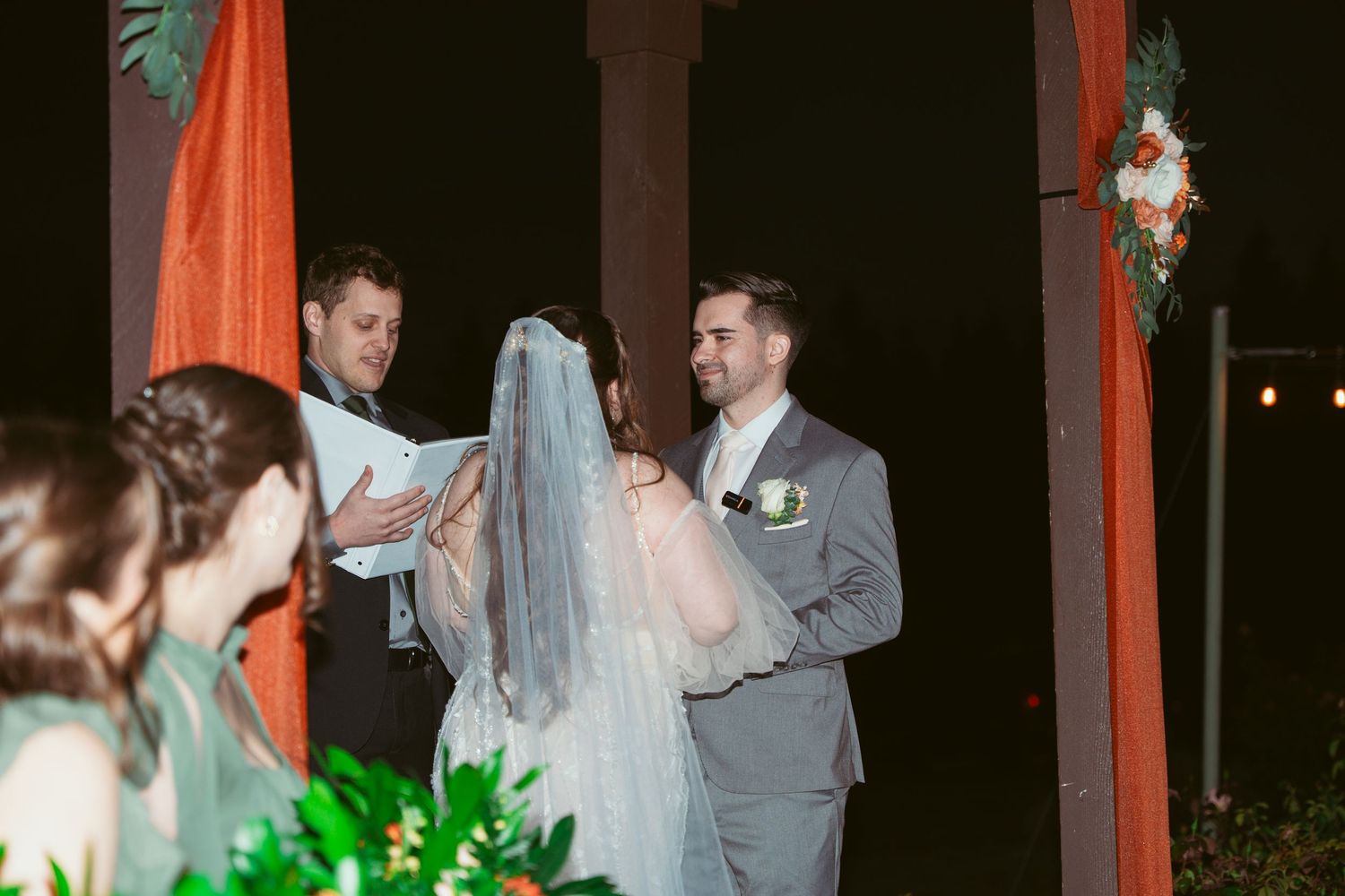 Wedding ceremony taking place under an illuminated outdoor pavilion with orange draping.