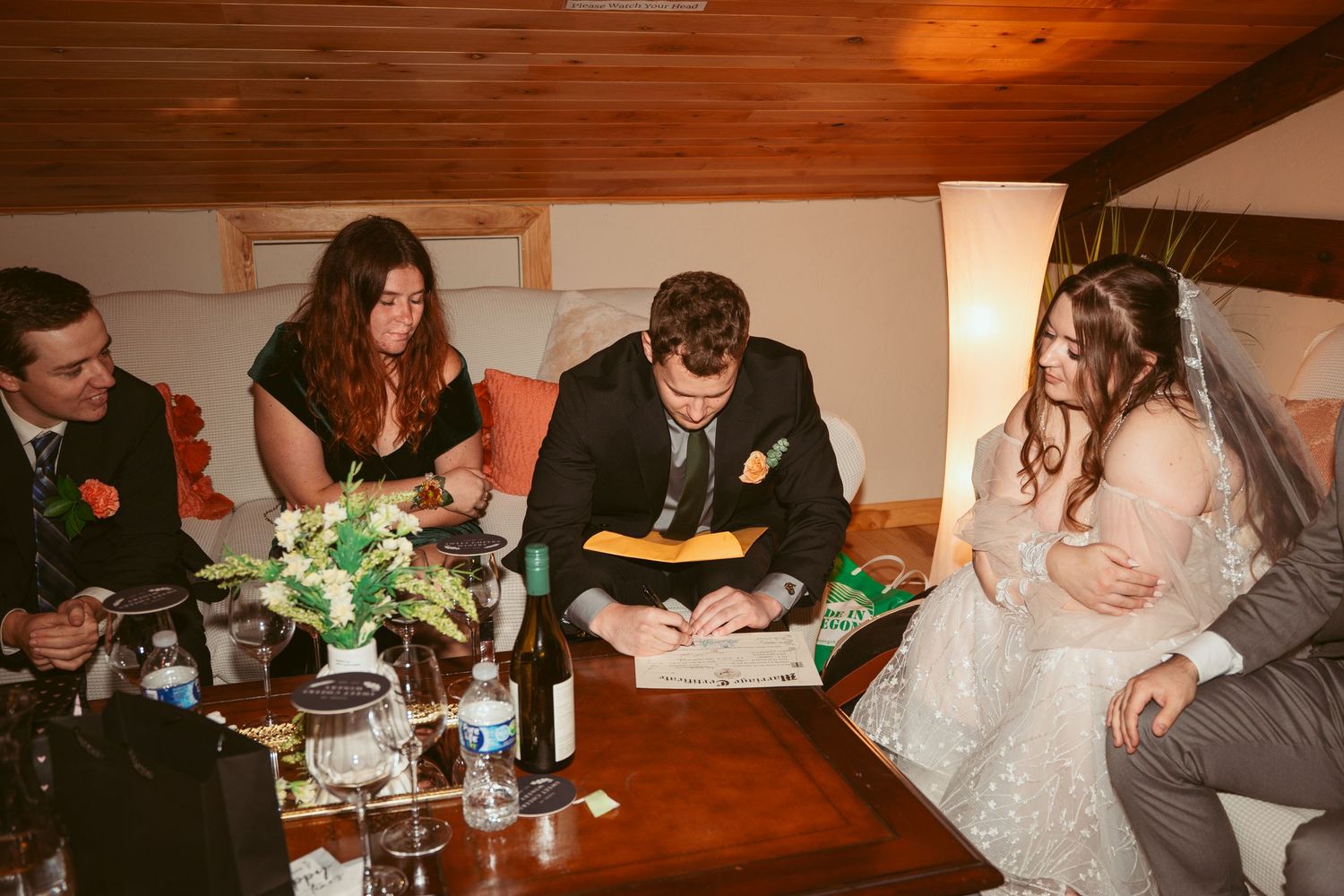 Wedding guests gather around wooden tables at an evening reception dinner.