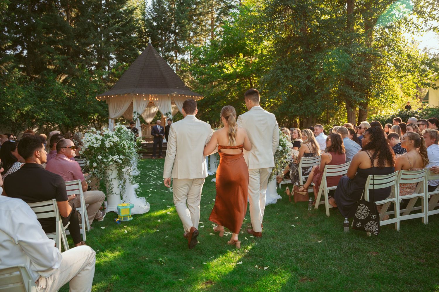 Outdoor wedding celebration with guests mingling on a sunlit lawn near a historic house.