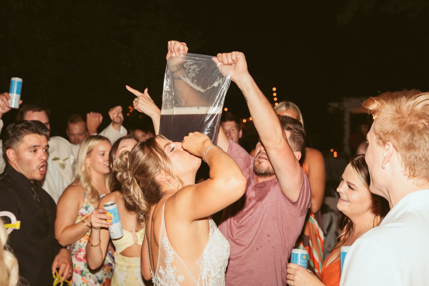 Party guests celebrating with drinks and raising a clear container in celebration at a nighttime event.